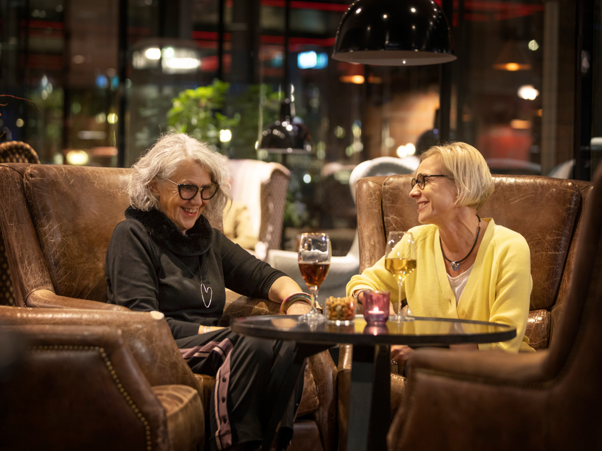 Two happy womens in brown chairs on a restaurant, drinking some wine. 