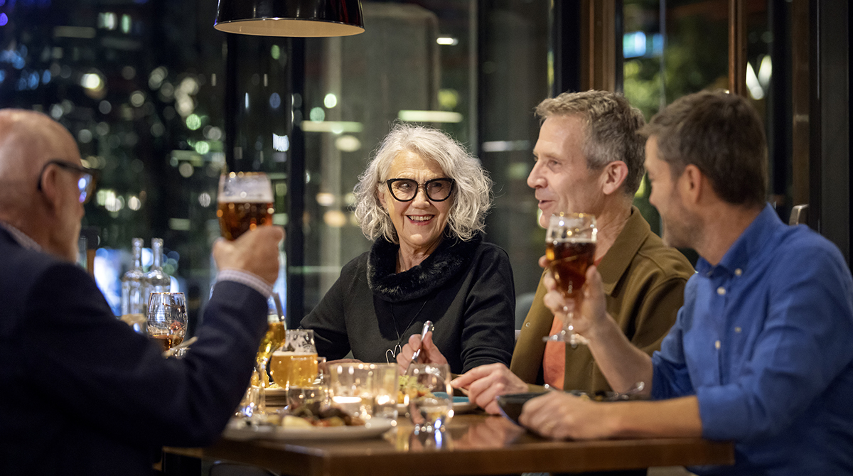 Four persons are sitting on a restaurant, drinking and eating some good food and having a nice time. 