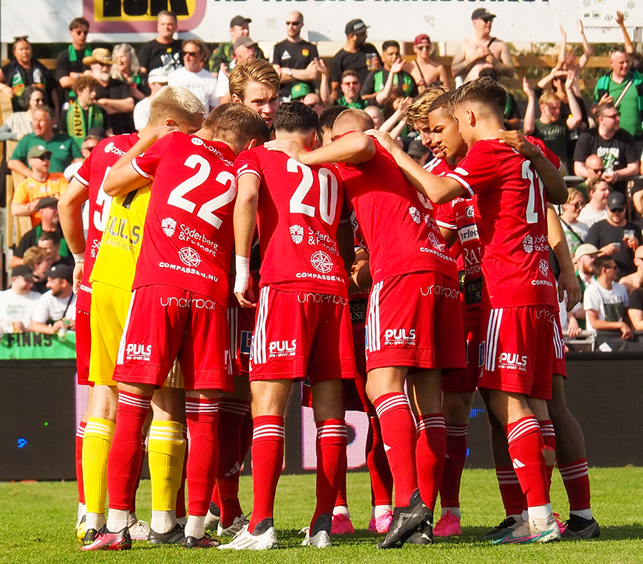 Football players dressed in red stand together on the football field in a ring.