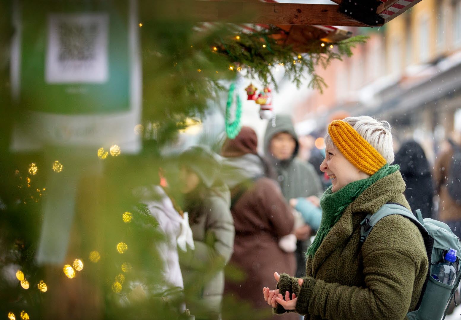 En kvinna i kort blont hår och gult stickat hårband står och kikar på saker vid ett marknadsstånd. 