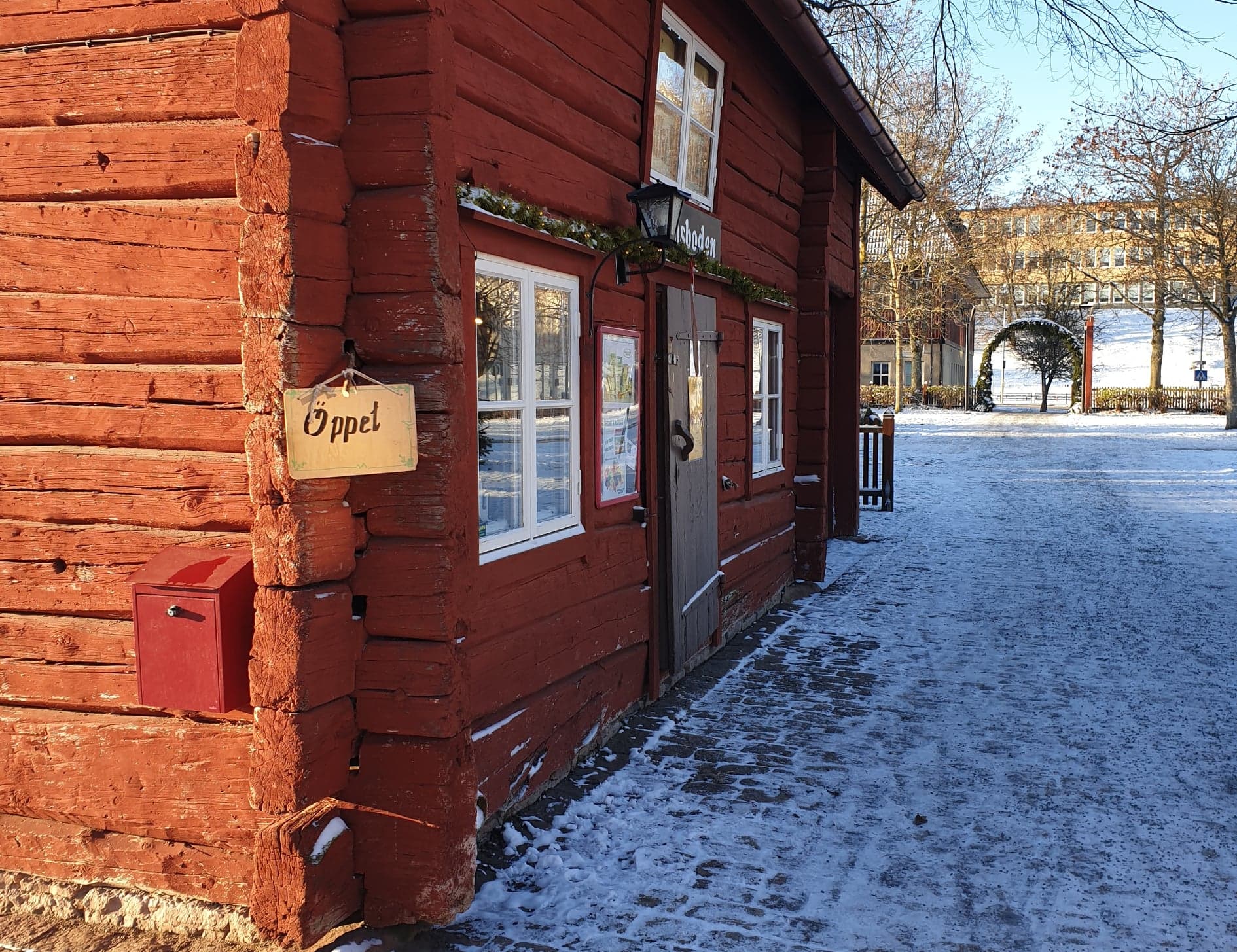 The facade of a red cottage. On the corner there is a small wooden sign saying "Open".