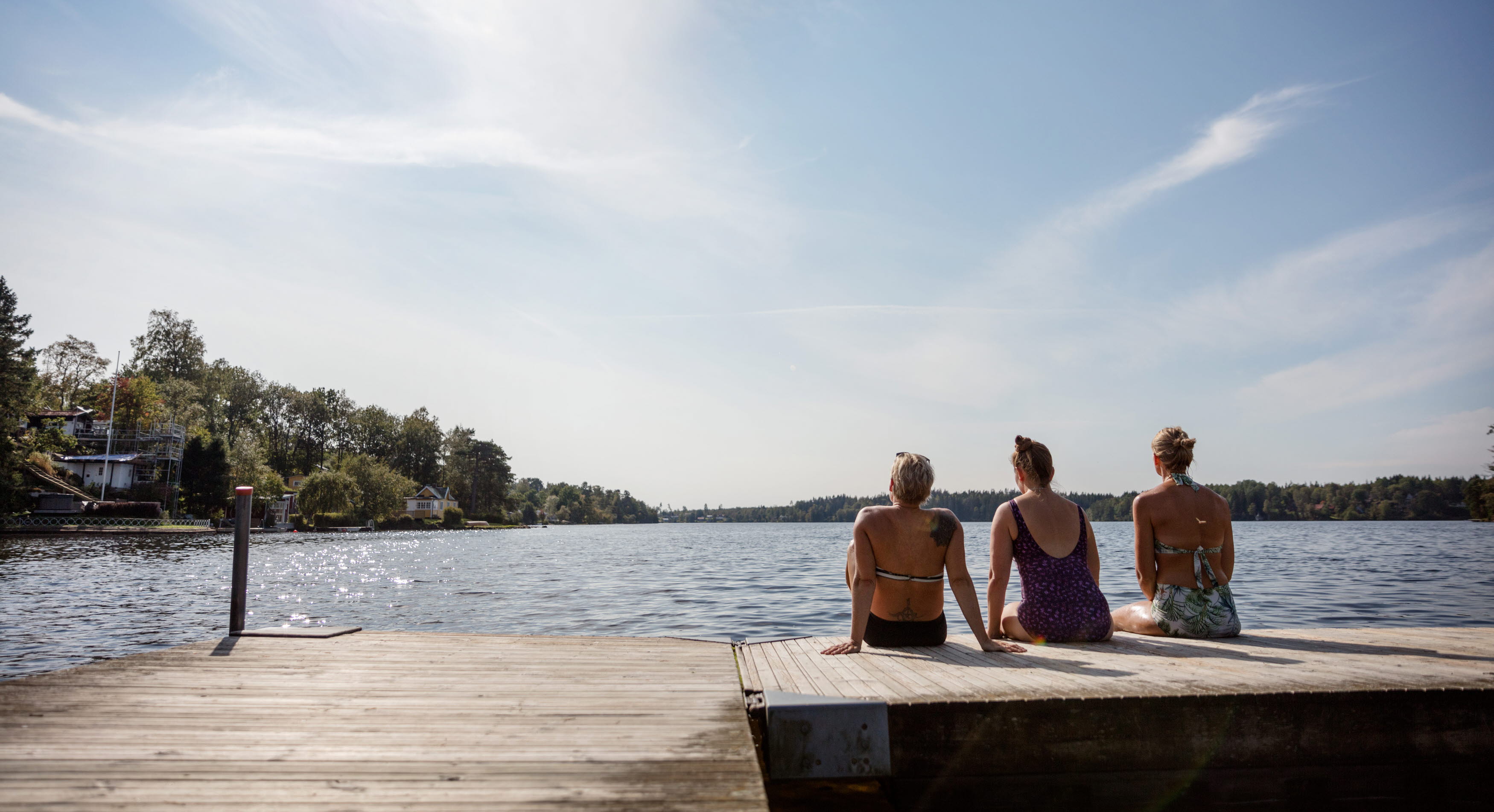 Tre kvinnor sitter på en brygga vid en sjö.