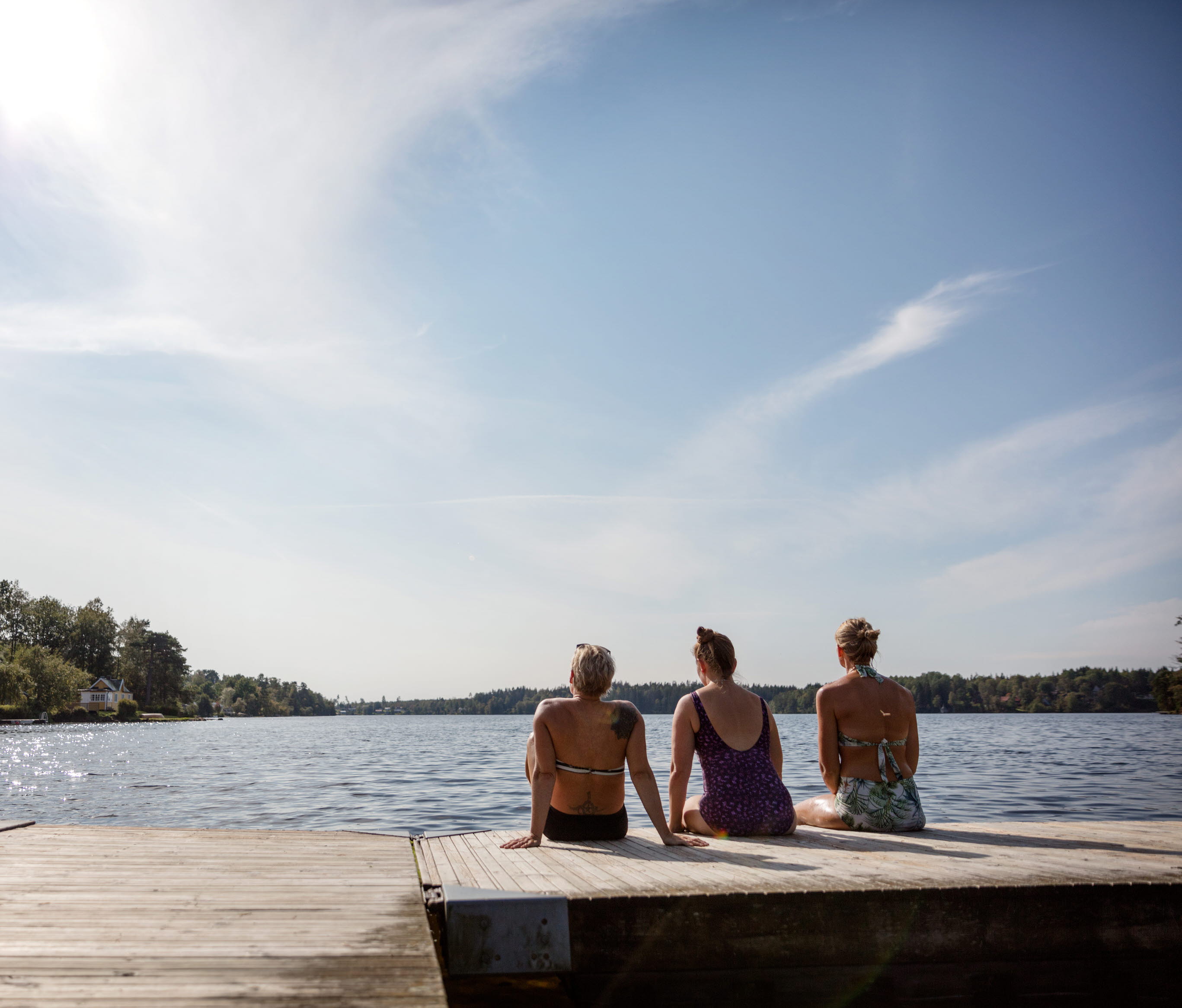 Tre kvinnor sitter på en brygga vid en sjö.