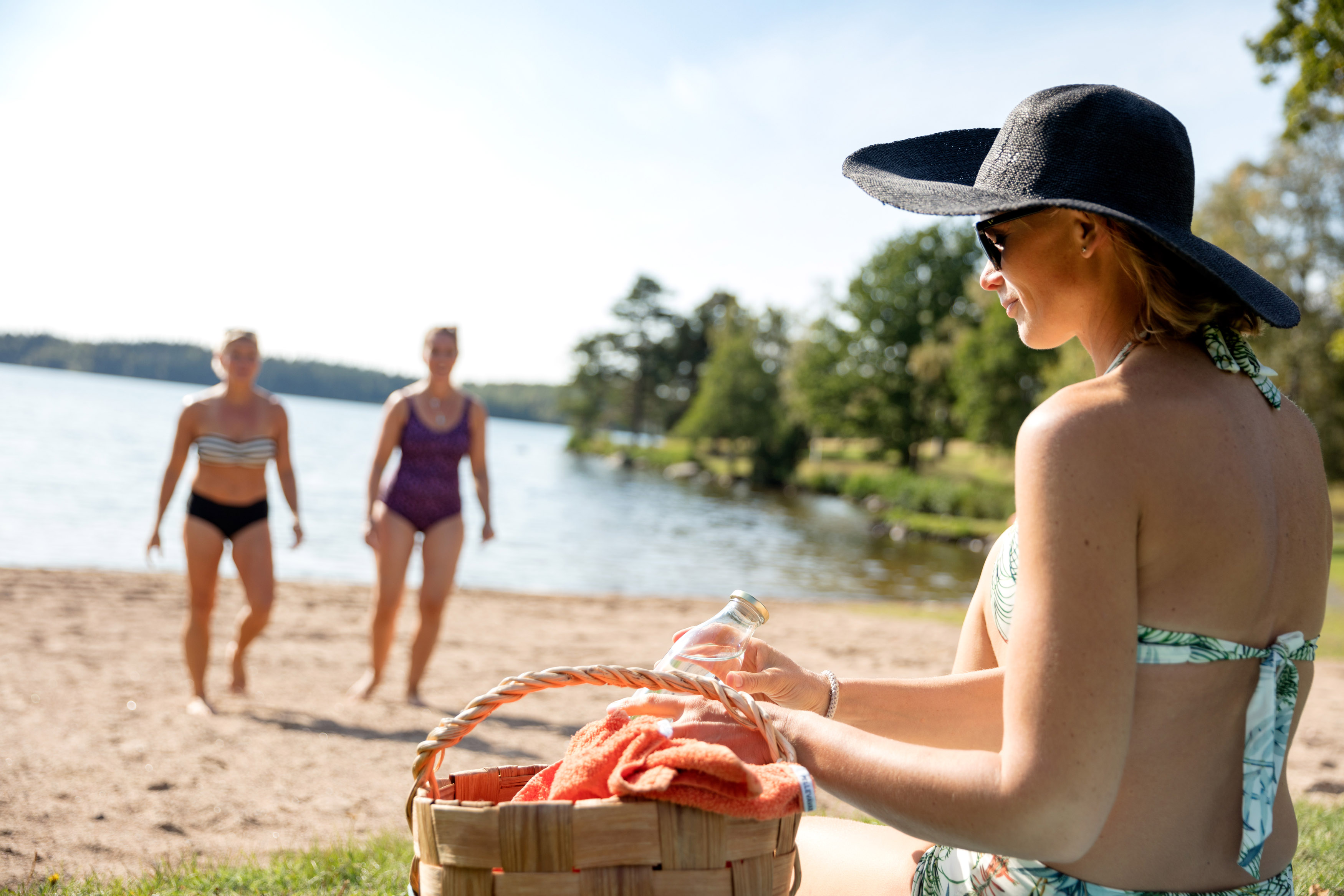Två kvinnor är påväg till en tredje som sitter och packar upp picknick ur en korg.