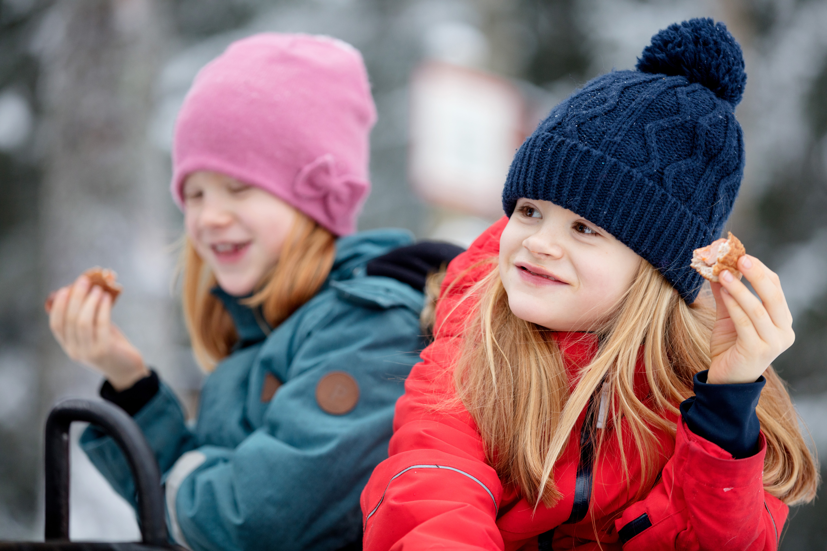 Family sitting by the fire surrounded by a winter landscape at Billingen moutain. Two girls are eating hot dogs. 