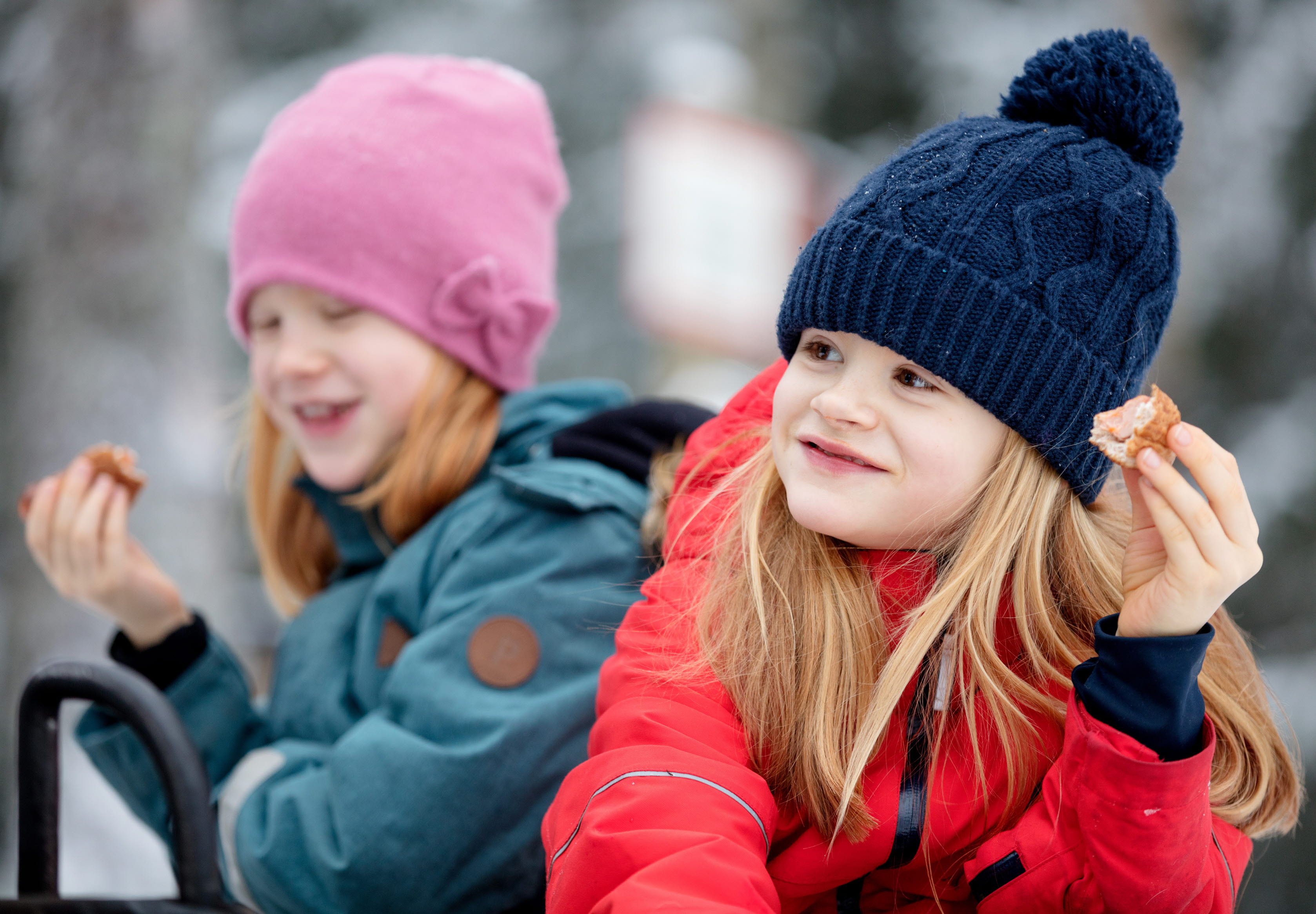 Familj som grillar i vinterlandskapet på Billingen.Två flickor sitter och äter korv.