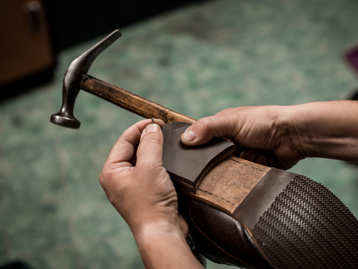 Två händer som håller i en sko med en hammare i ena handen. 