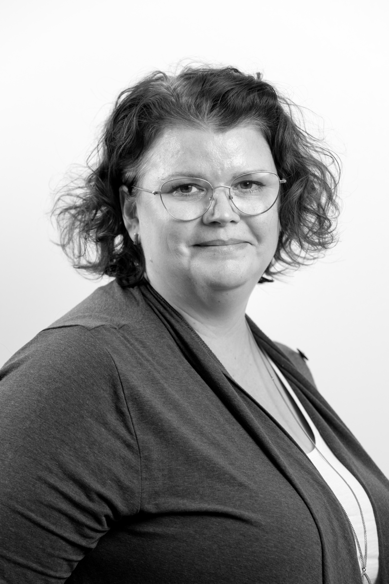 Kvinna med kort, mörkt och lockigt hår. Hon bär diskreta glasögon och en mörk kofta över en ljus tröja.  