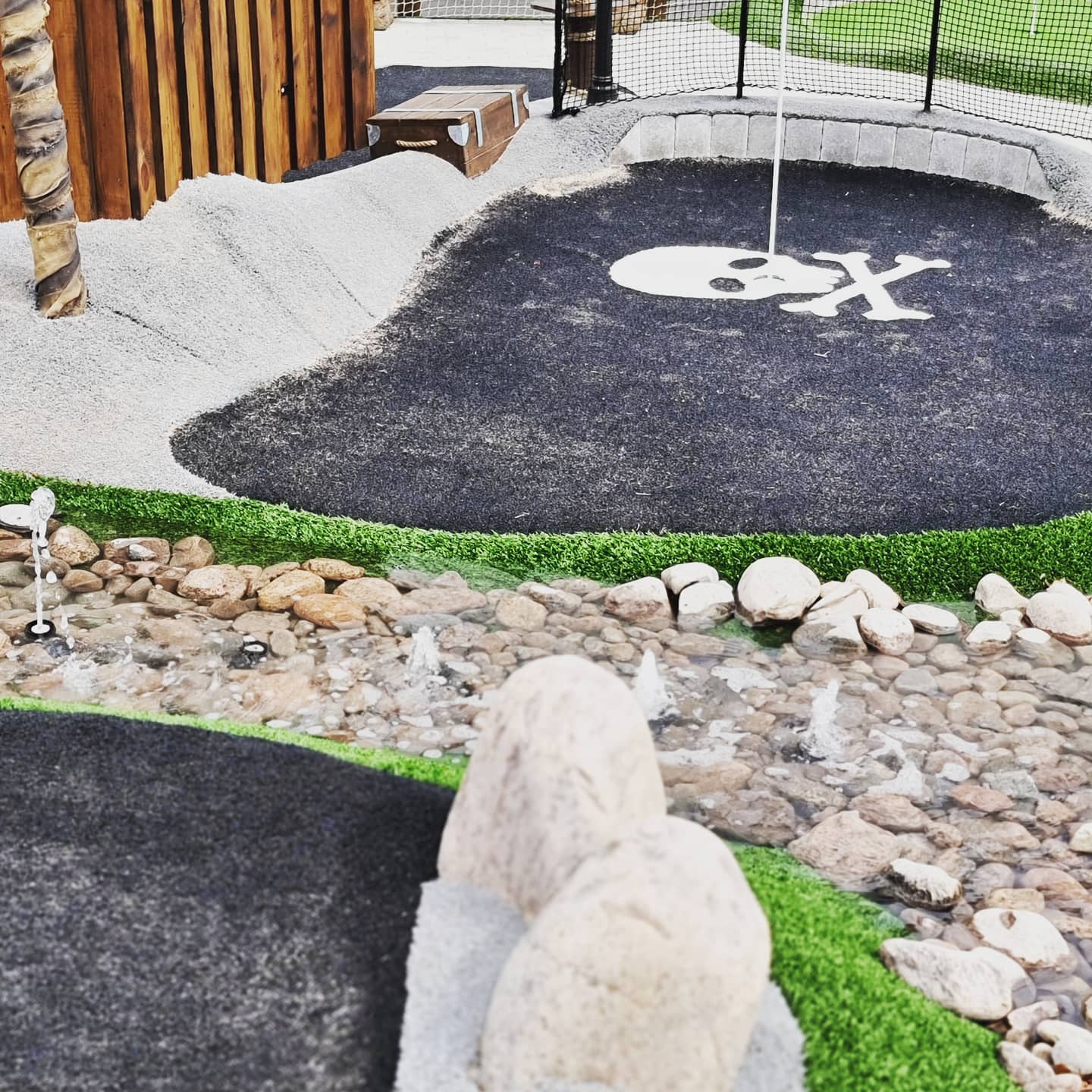 Detaljbild på en äventyrsgolfbana där hålet för bollen är i en bild av en dödskalle. 