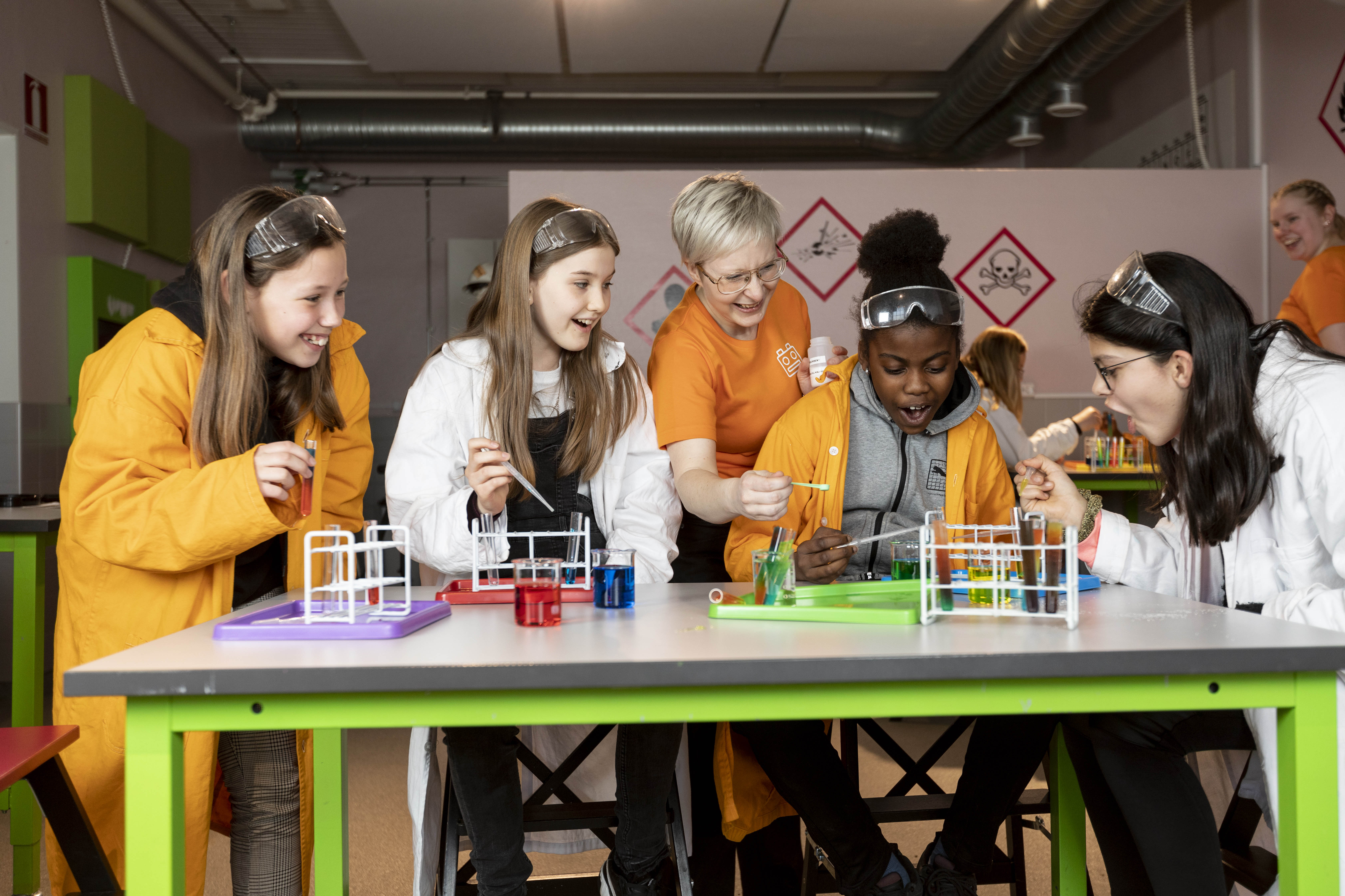 Fyra flickor och en pedagog som experimenterar runt ett bord i ett labb.