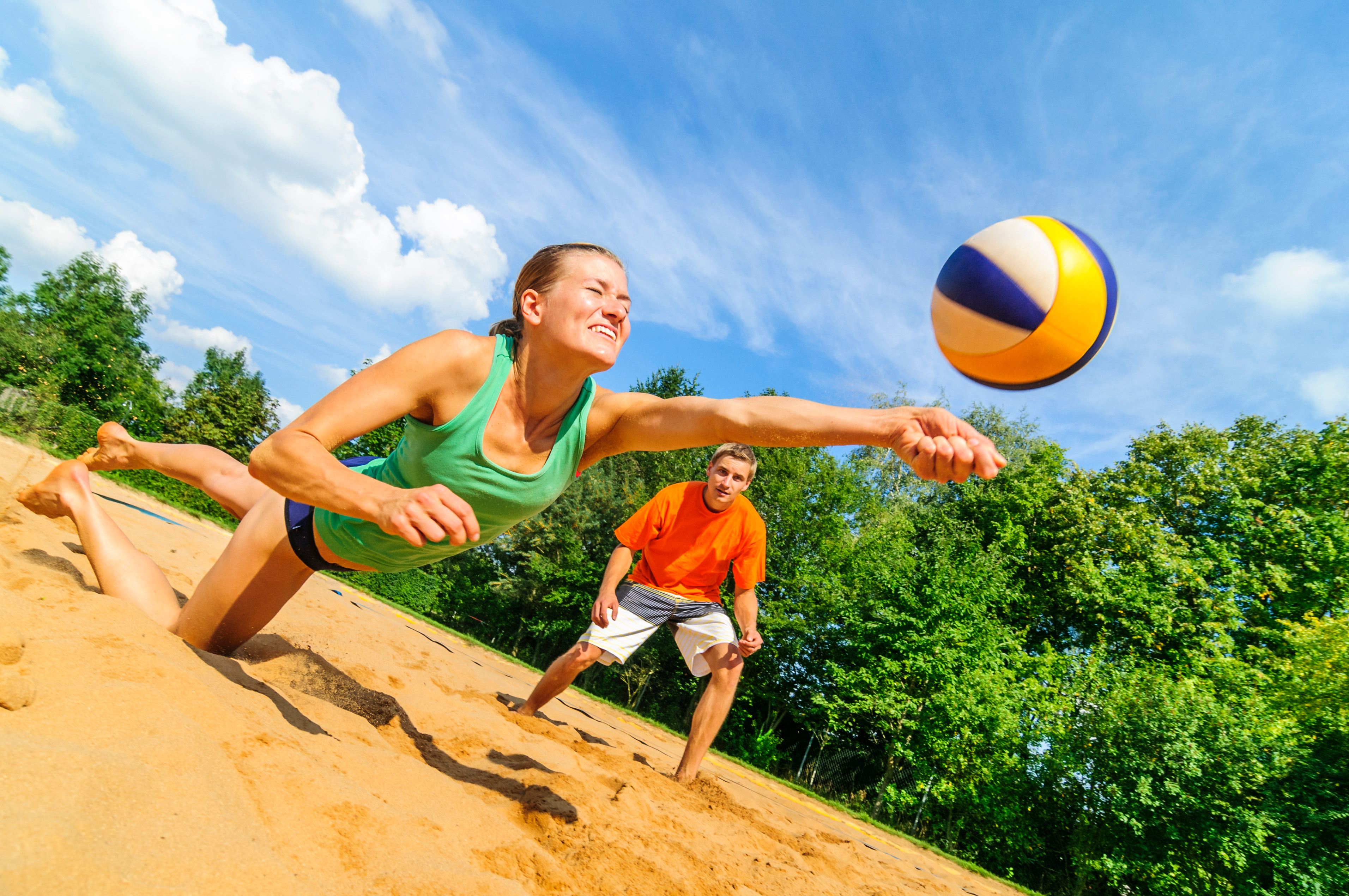 Kvinna som slänger sig för att ta bollen i beacholley. En man syns i bakgrunden.
