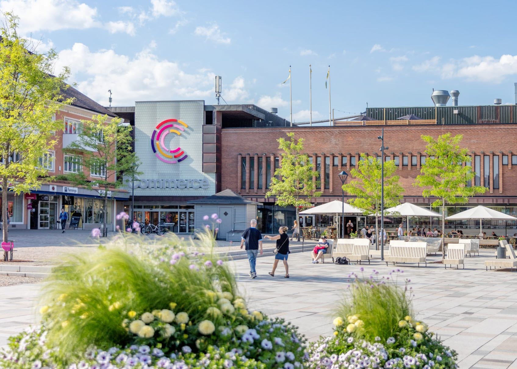 En bild på Hertig Johans torg med blommor i förgrunden och Commerce i bakgrunden. 