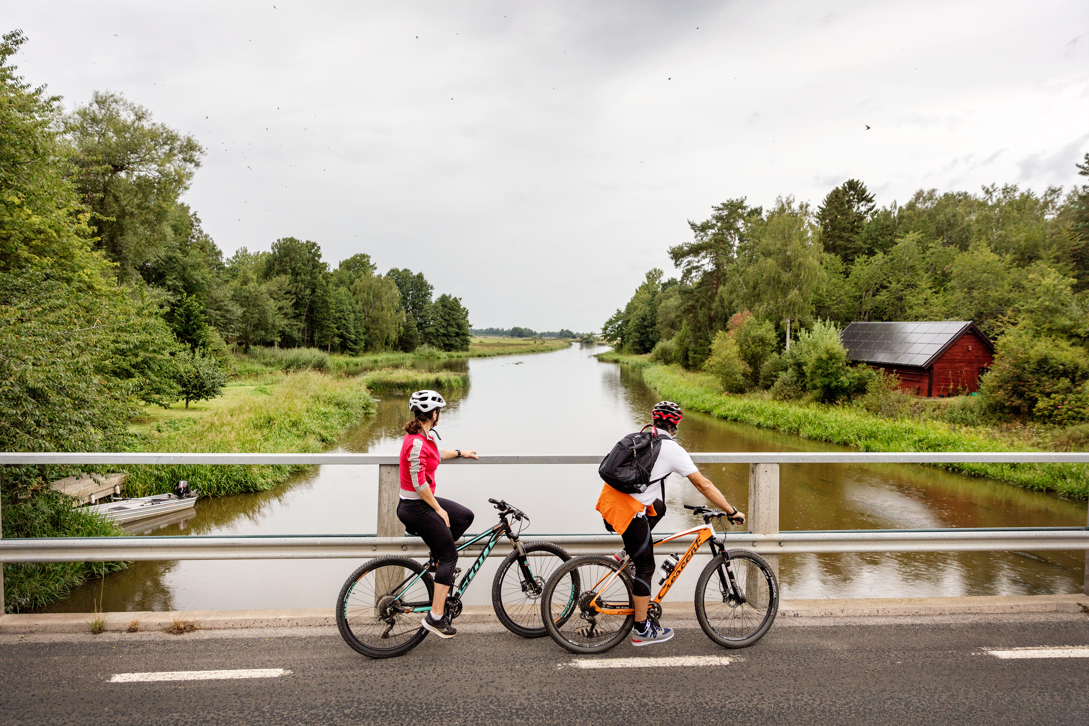 Två cyklister har stannat på en bro för att titta på ån som flyter under dem.