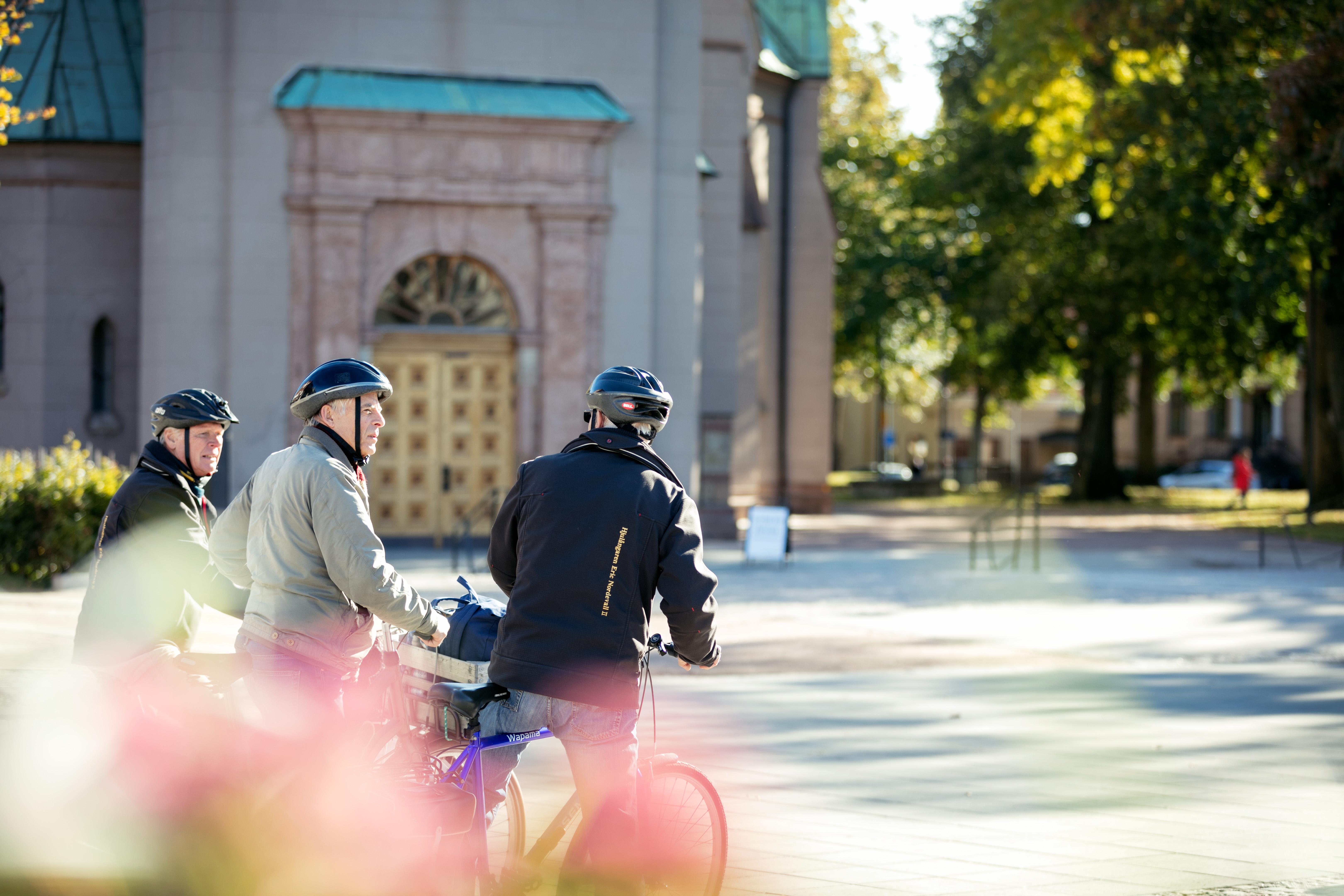 Tre män på cyklar med står utanför en kyrka och pratar. 