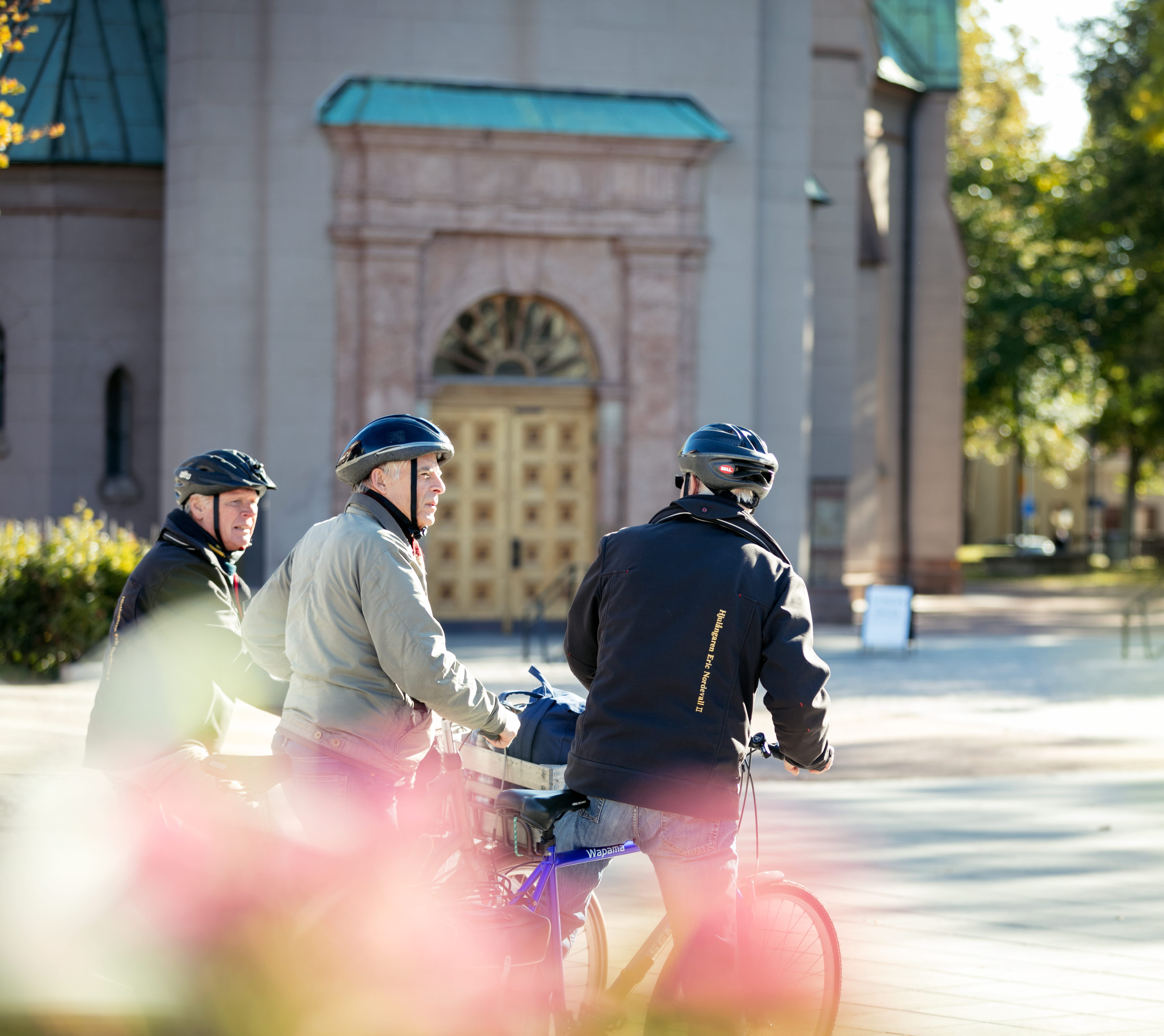 Tre män på cyklar med står utanför en kyrka och pratar. 