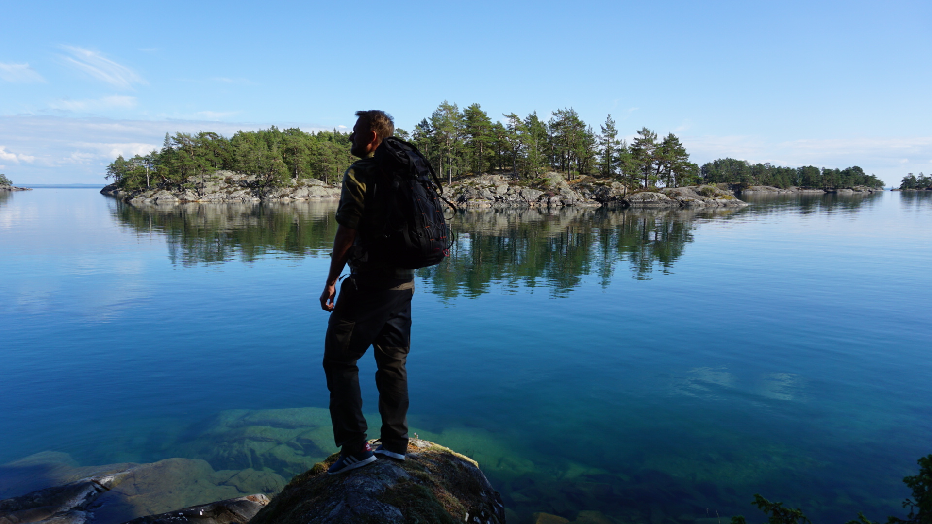 The silhouette of a man standing on the edge of a cliff gazing out over the clear blue water.