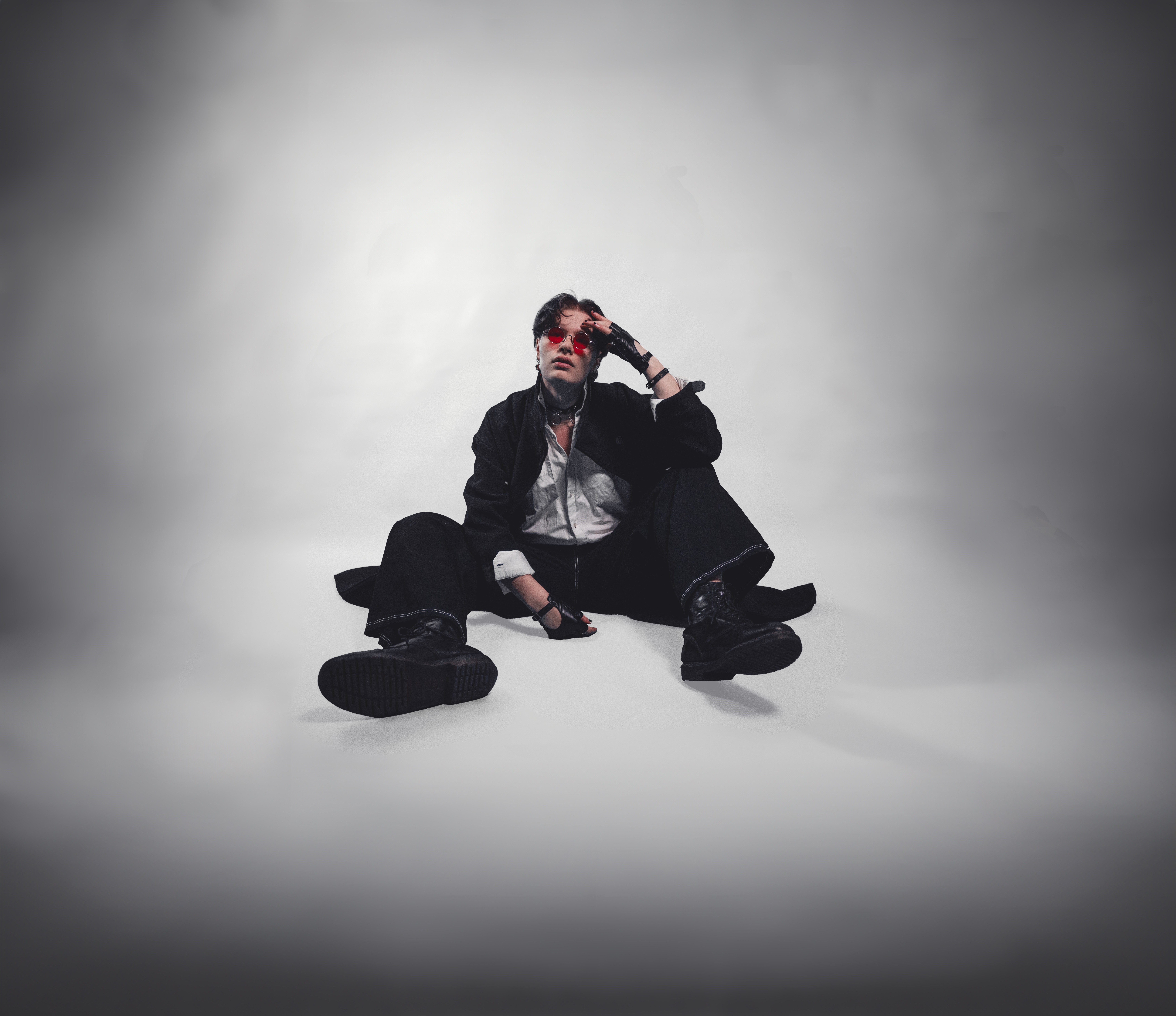 En kille i svart klädsel och solglasögon sitter på golvet