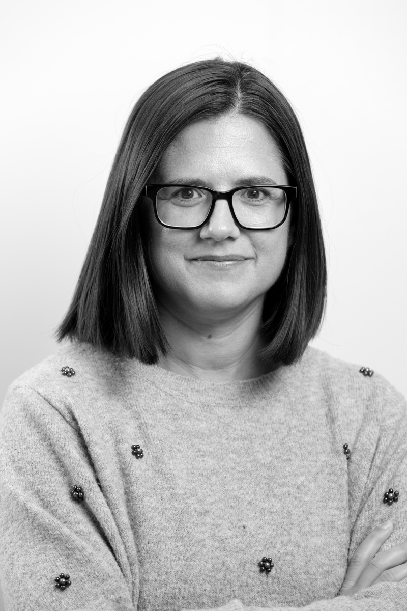 Bild av en kvinna med kort mörkt hår och fyrkantiga glasögon. Hon bär en stickad tröja med små blommor gjorda av pärlor. 