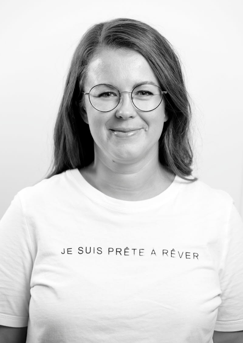 Bild på kvinna i mörkt hår och runda glasögon och ljus tröja.