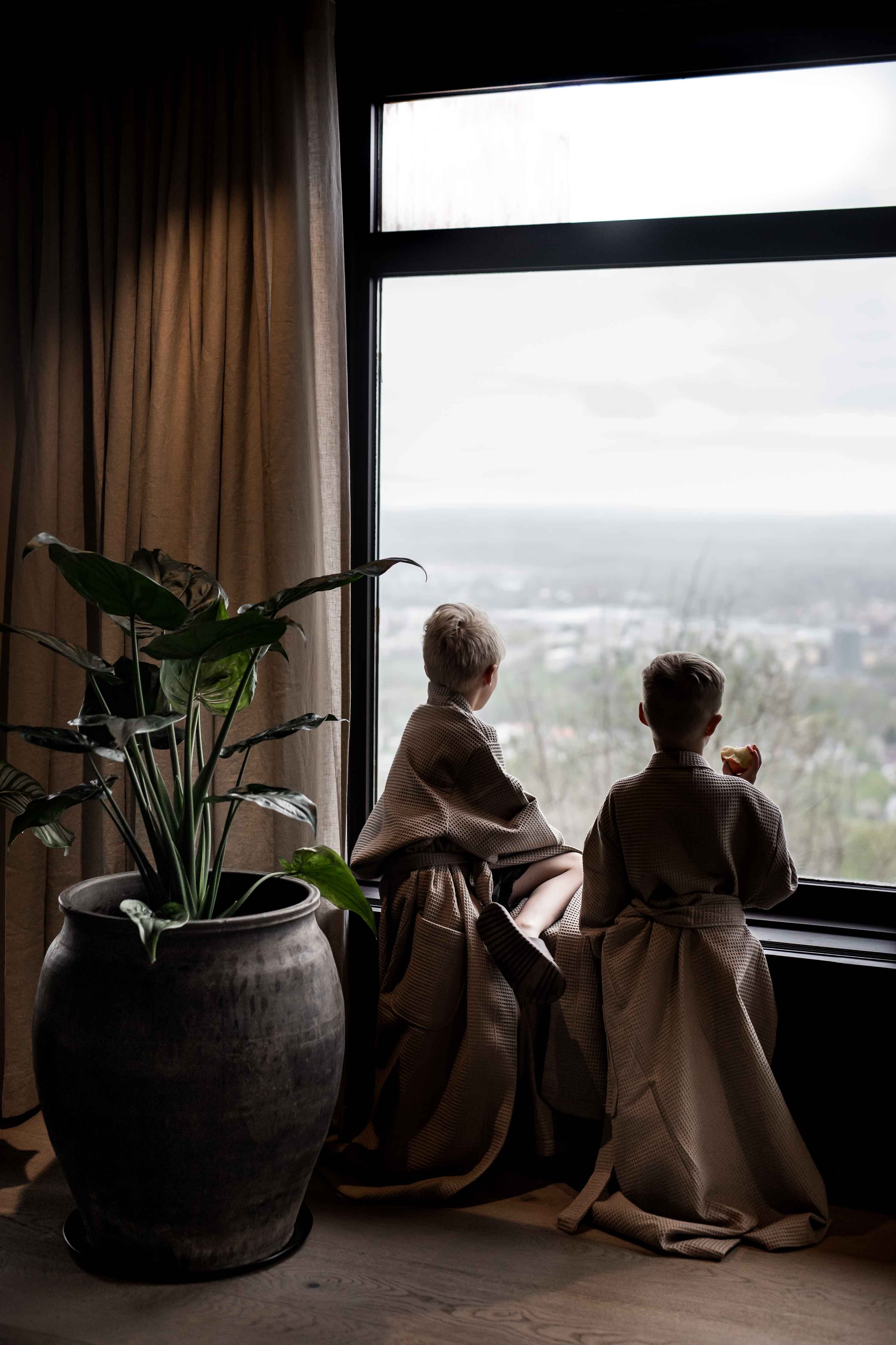 Två barn i badrockar vid fönster och tittar ut över utsikten. 
