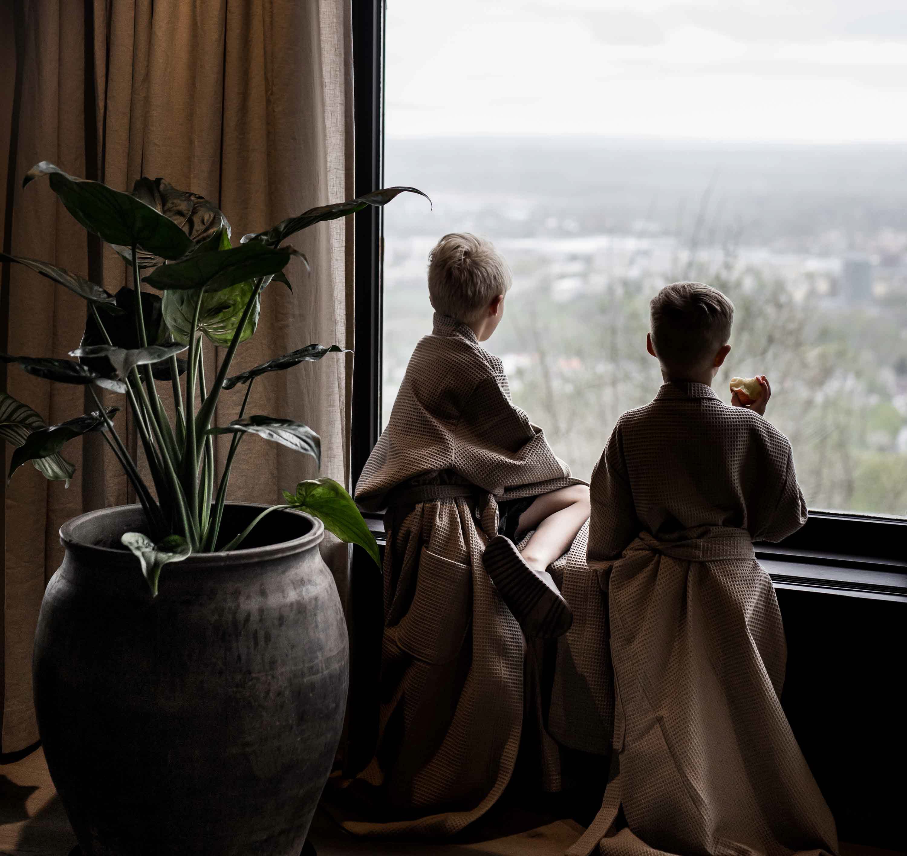 Två barn i badrockar vid fönster och tittar ut över utsikten. 