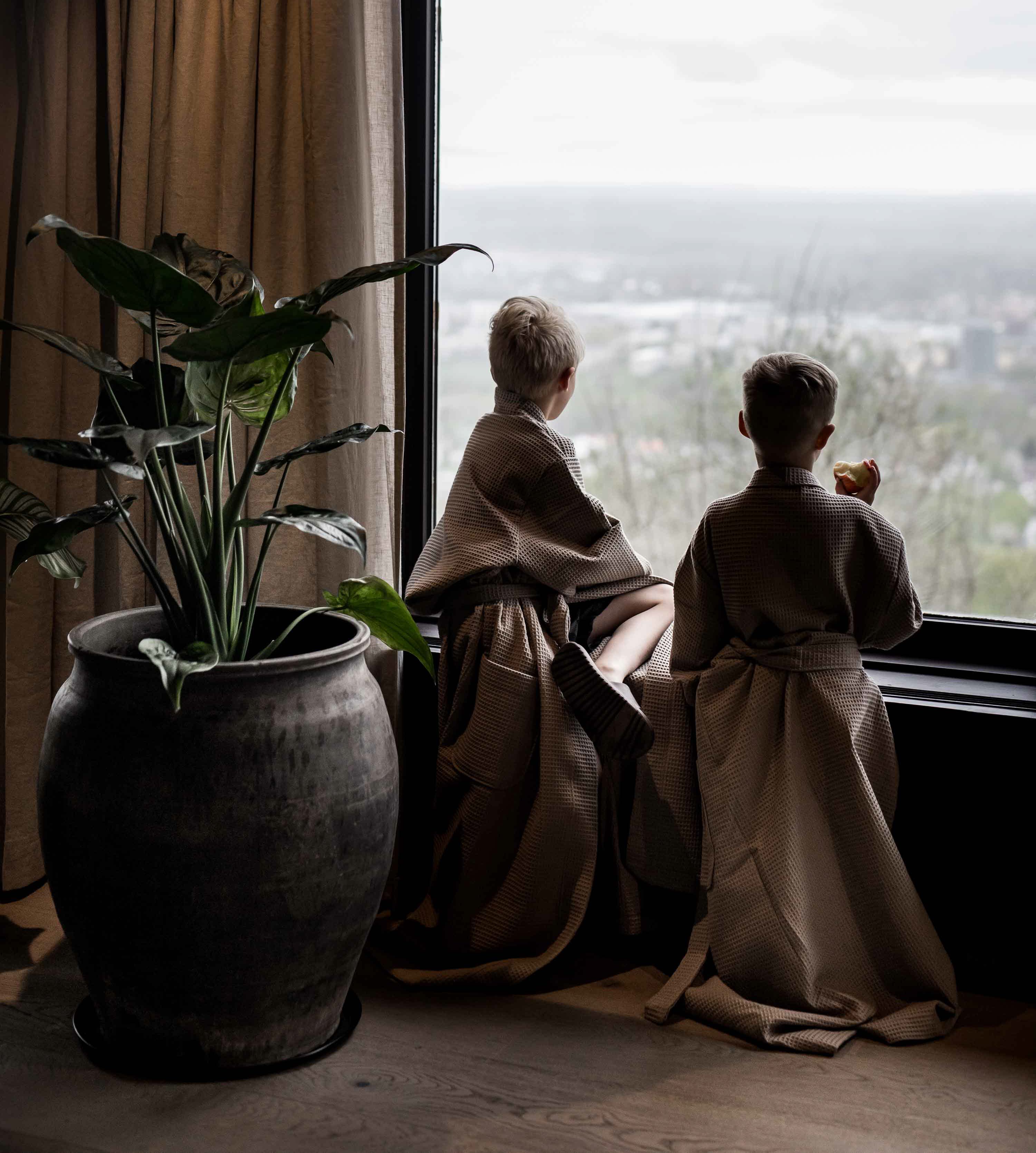 Two children in bathrobes by the window and looking out over the view.