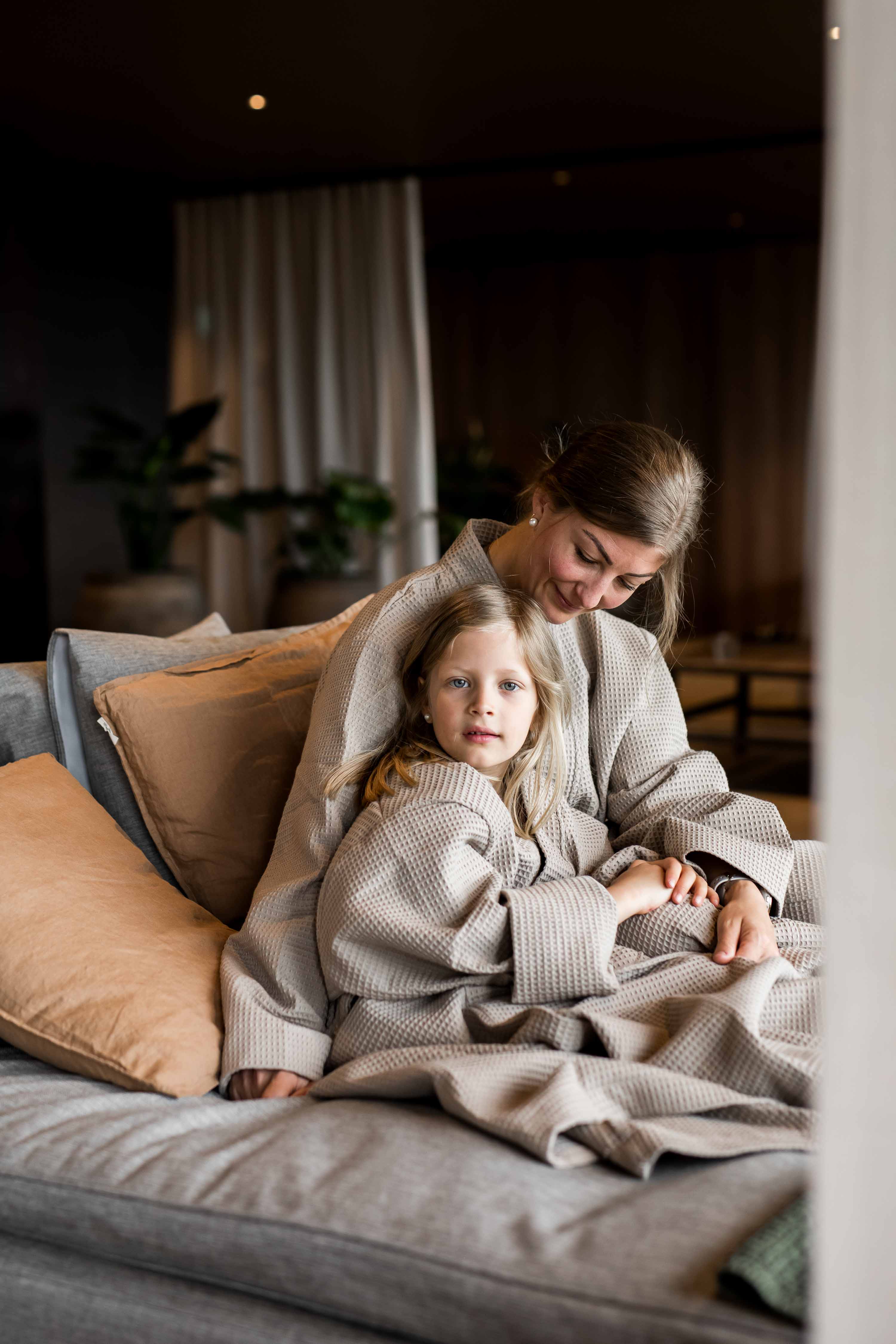 Kvinna och barn sittandes i en säng intill varandra, kvinnan tittar ner på barnet medan barnet kikar in i kameran.
