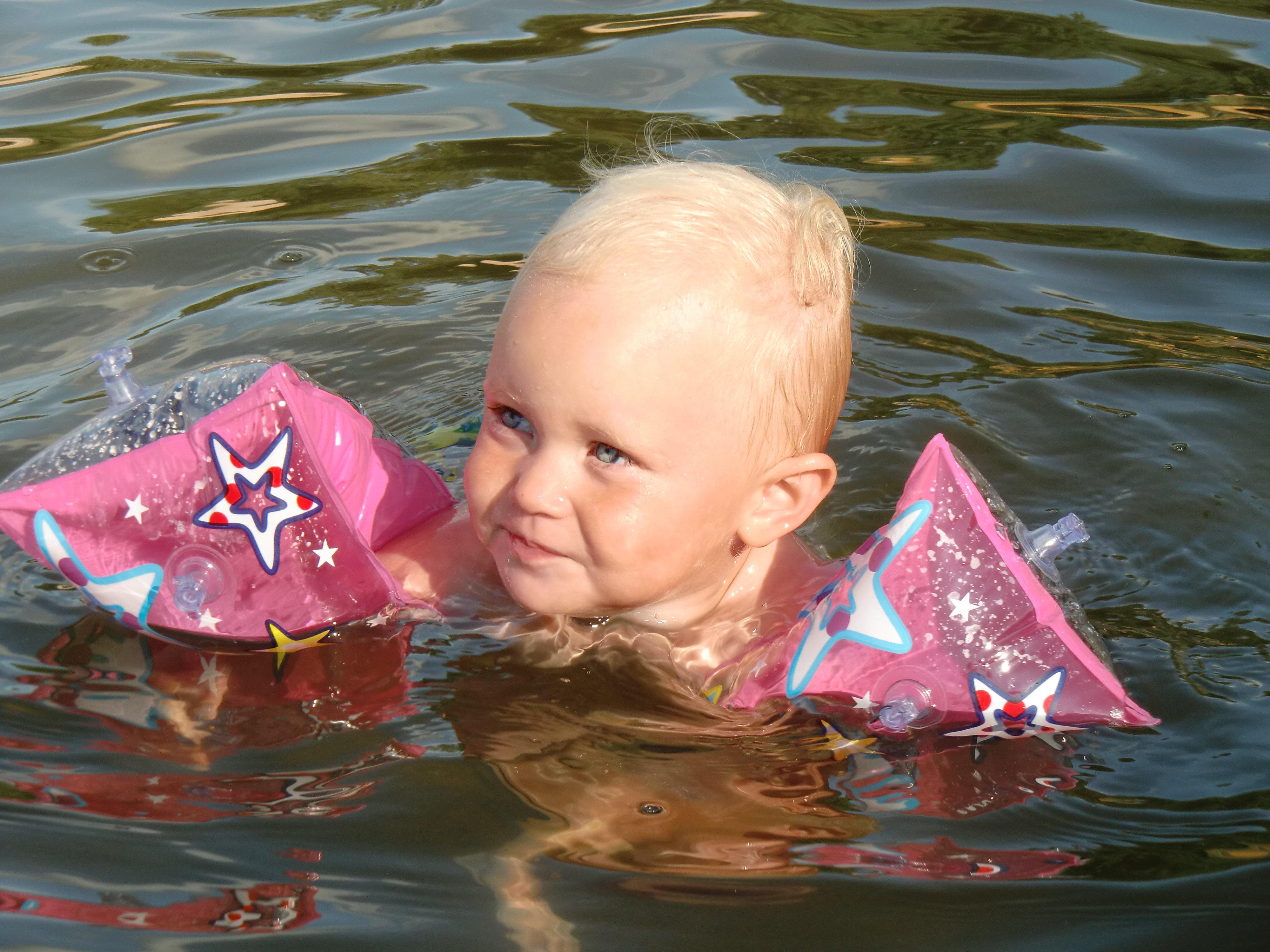 Liten flicka med rosa badpuffar badar i sjön.