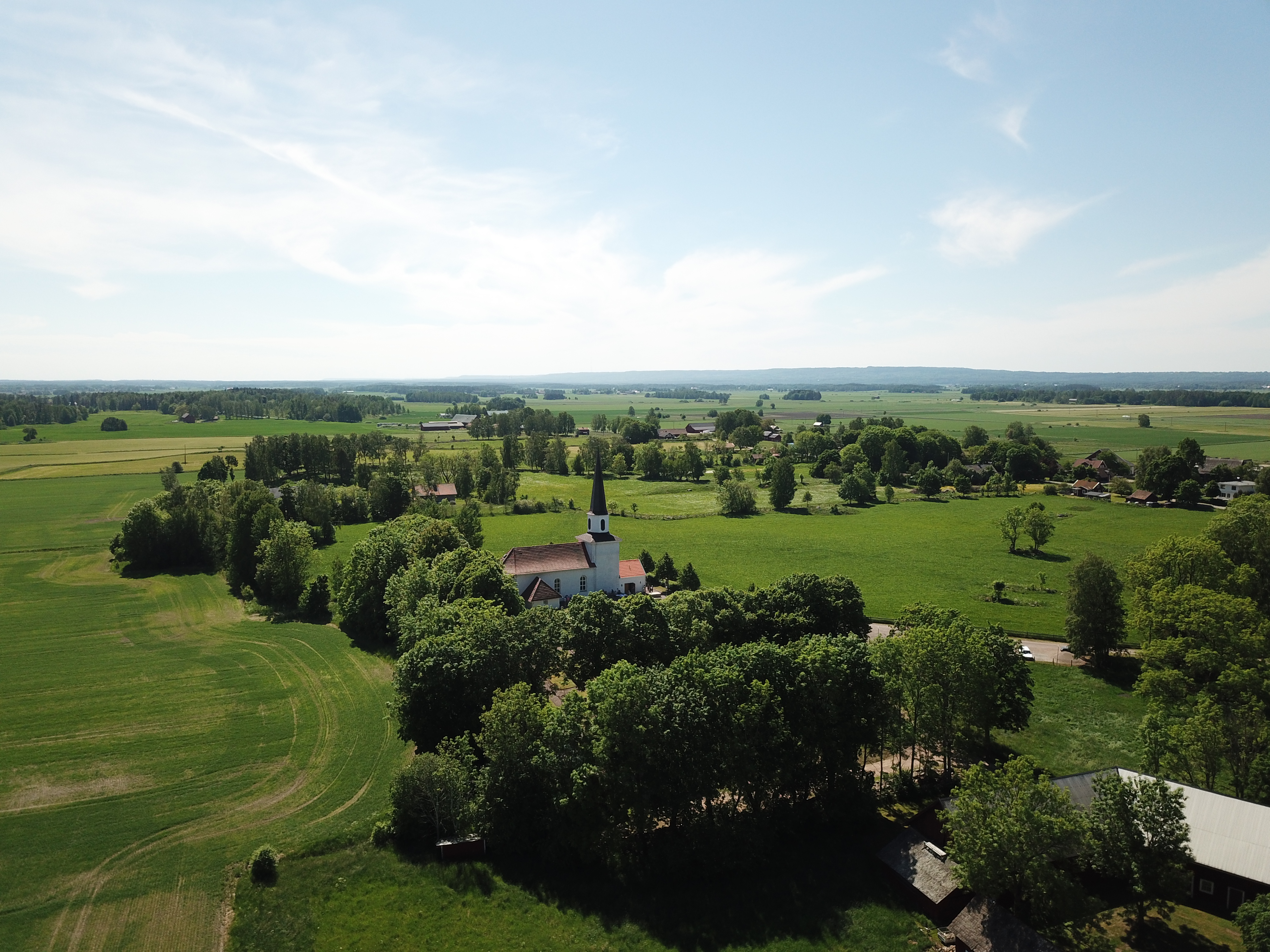 En vit kyrka i lummig omgivning med utsikt över nejderna. 