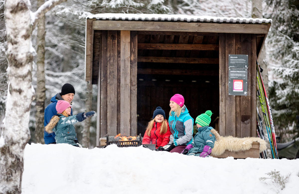 En familj sitter vid ett vindskydd ute i snön
