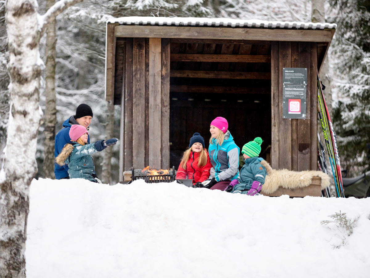 En familj sitter vid ett vindskydd ute i snön