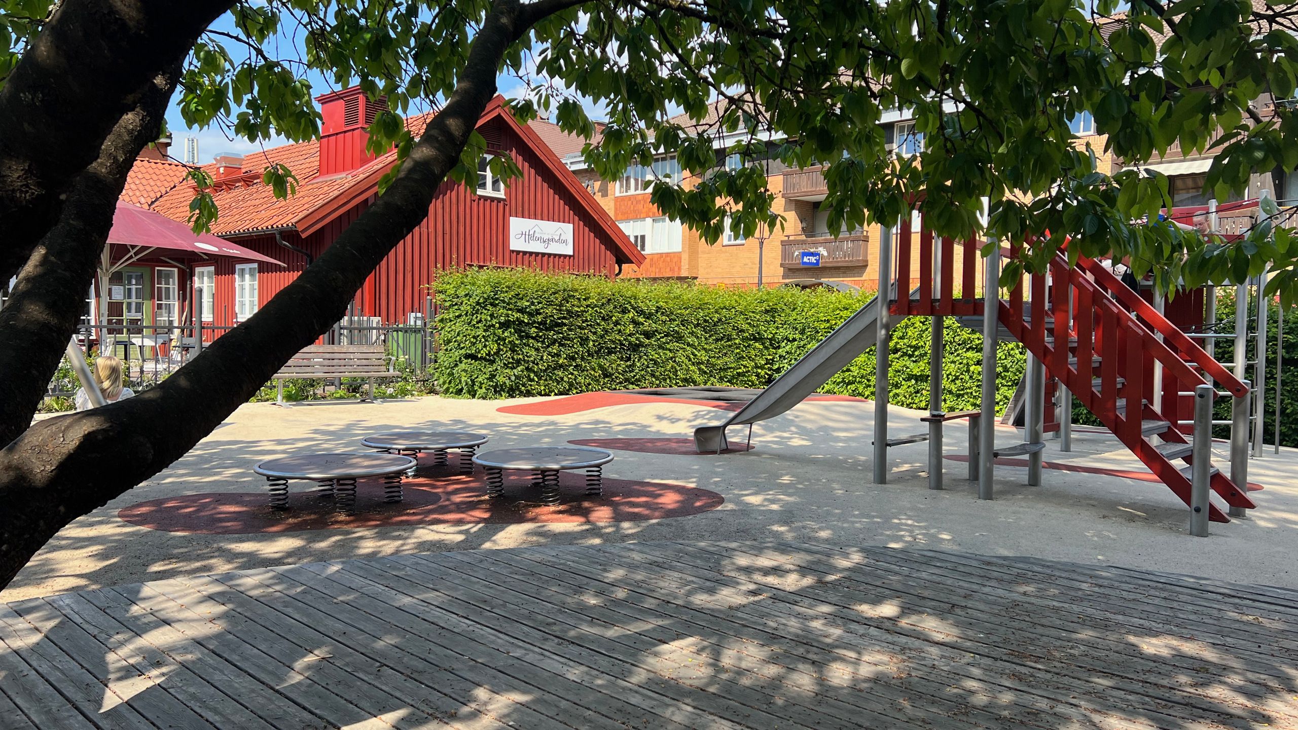 I förgrunden ett träd och i bakgrunden en lekställning och rött hus. 