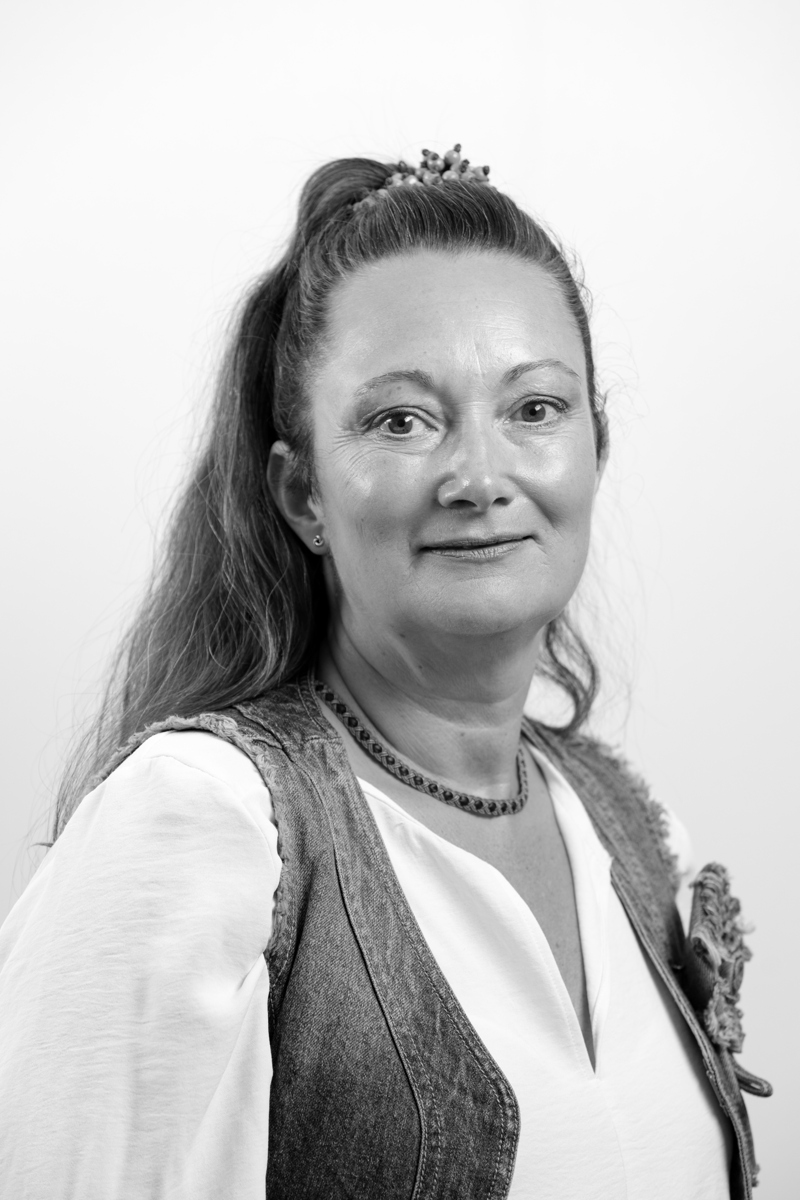 Bild av en kvinna med uppsatt långt mörkt hår. Vit blus och jeansväst. 