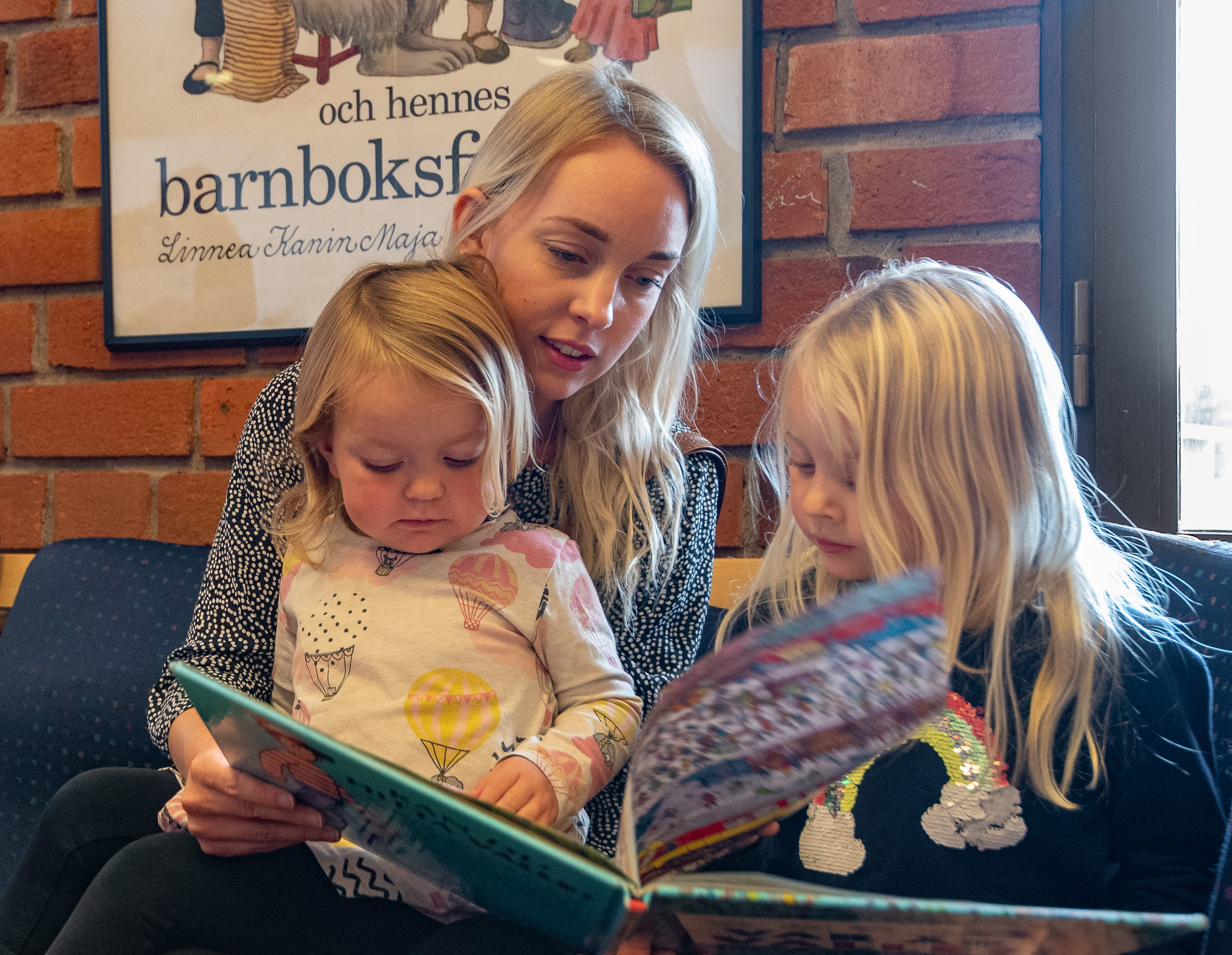 En kvinna och två barn sitter sitter i en soffa och läser böcker.