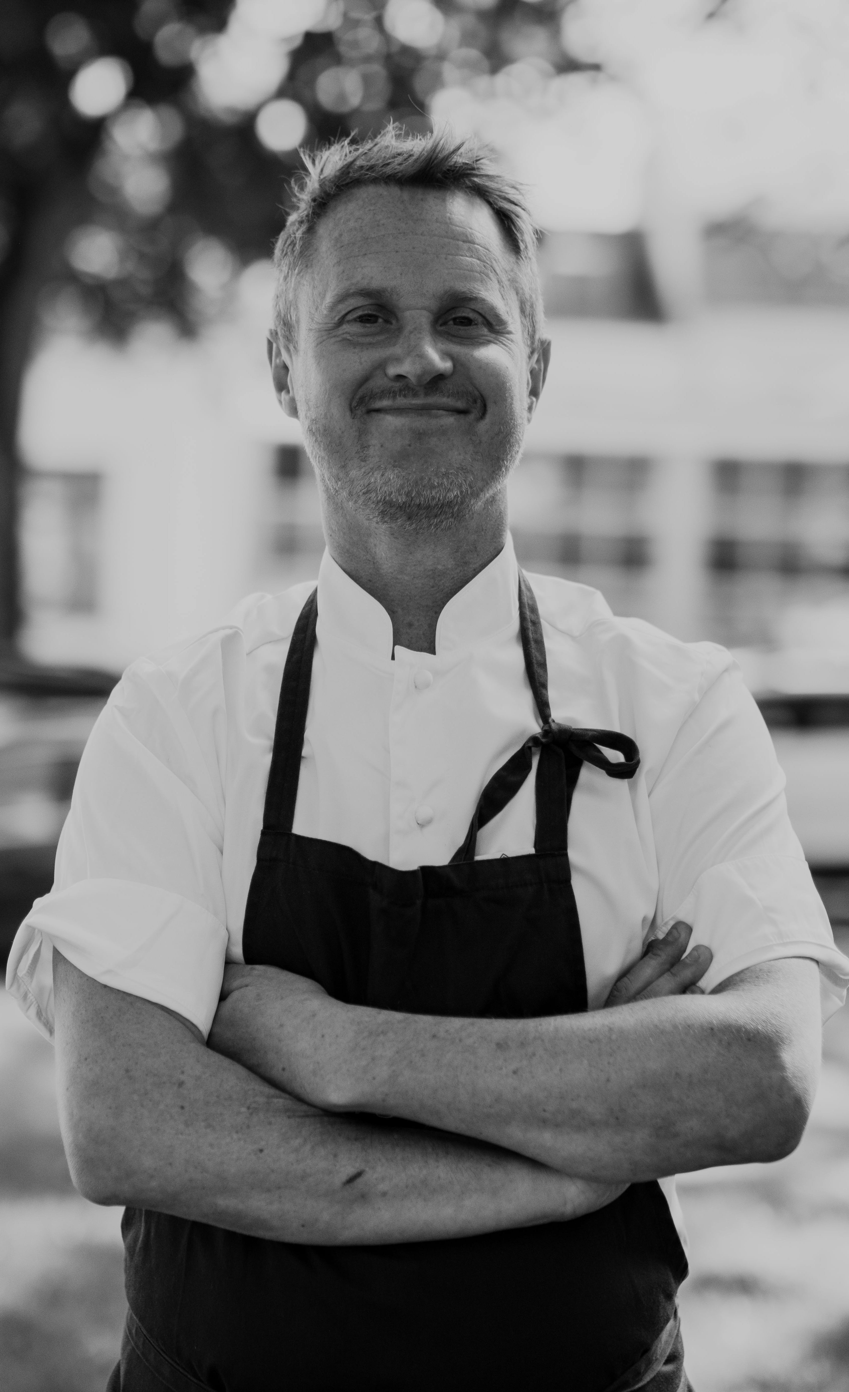 Ett porträtt på krögaren Karl-Johan Beckman i vit kockskjorta och svart förkläde. 