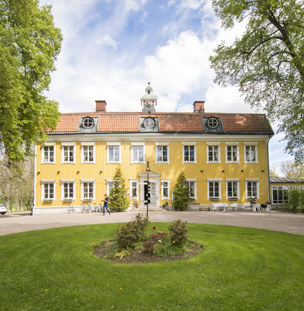 Ett stort gult hus i vackra lummiga omgivningar.