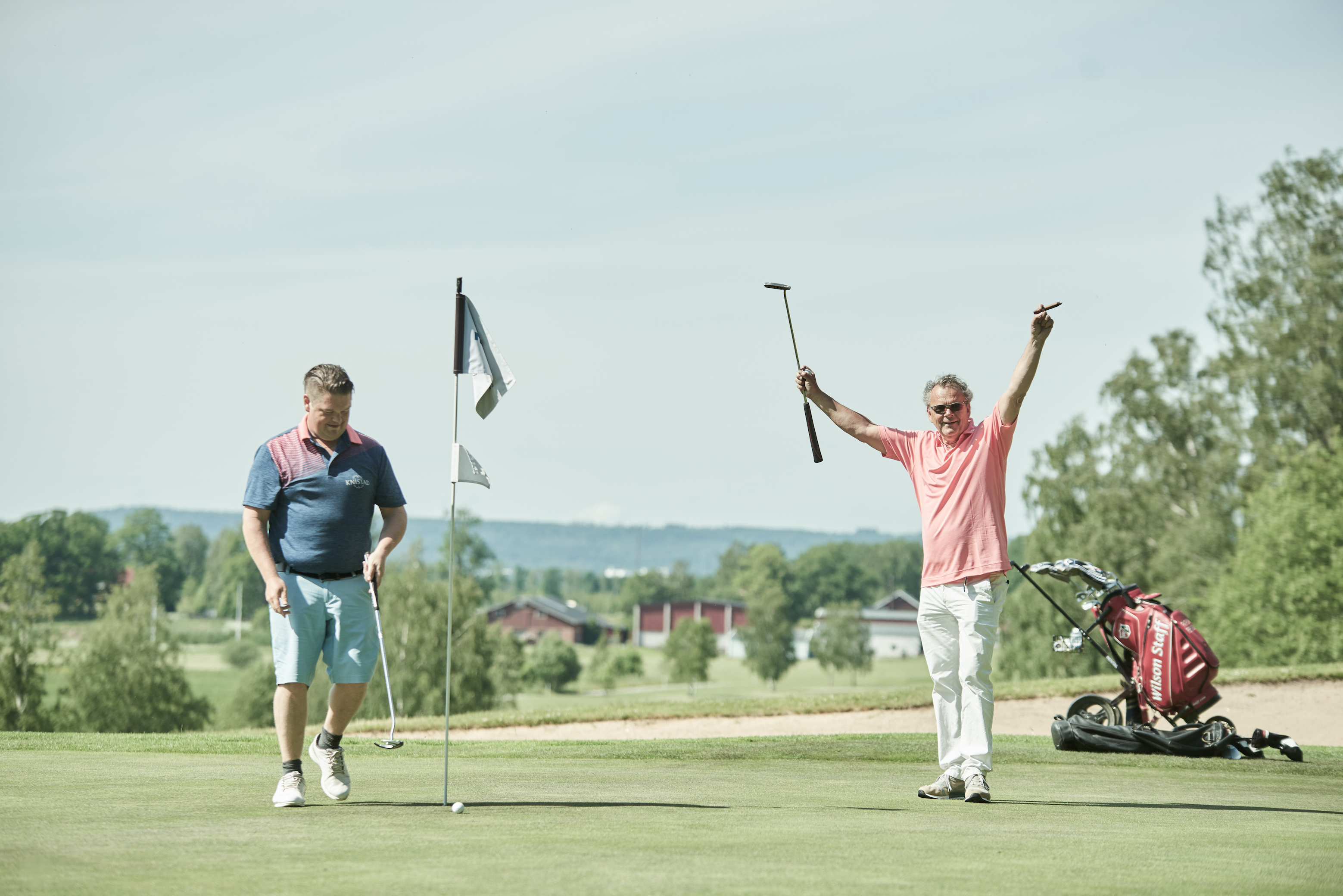 Två personer i bild, en av dem som är Steffo Törnkvist sträcker armarna i en jublande gest, den andra ska strax slå en golfboll.