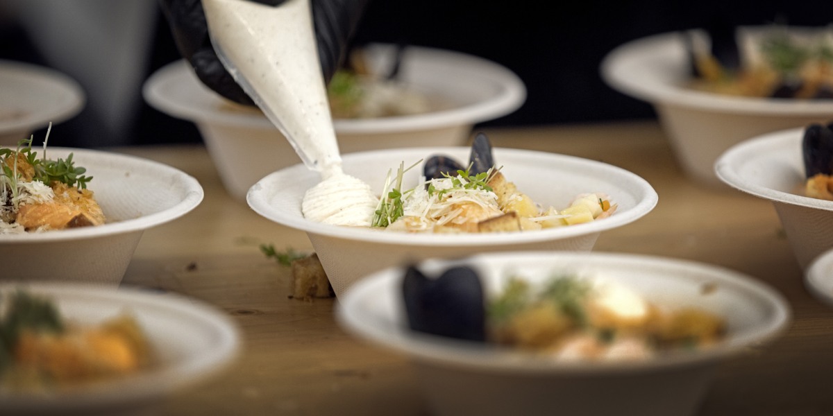 Flera djupa tallrikar och en hand med en sprits med kräm i som spritsas ut på en tallrik. 