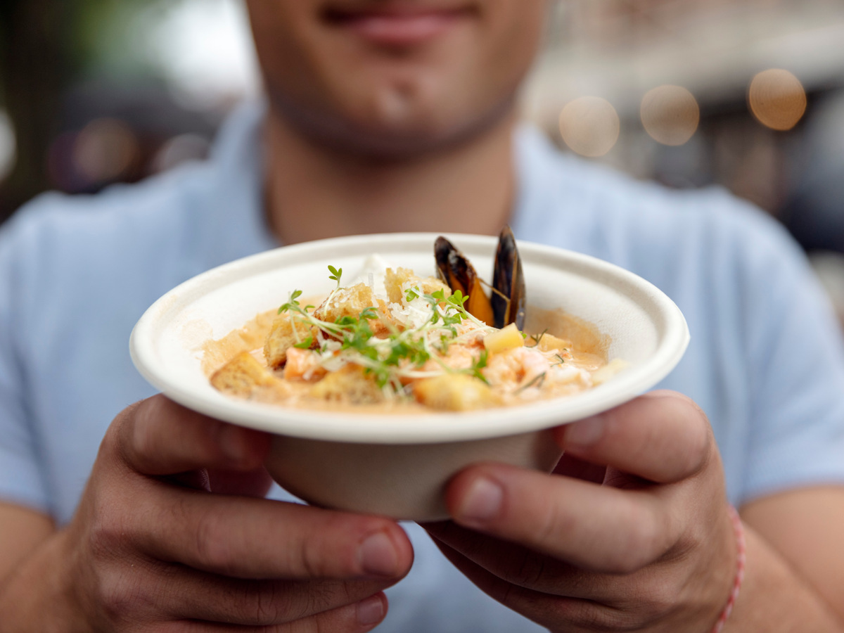 En man håller fram en djup tallrik med skaldjursgryta. 