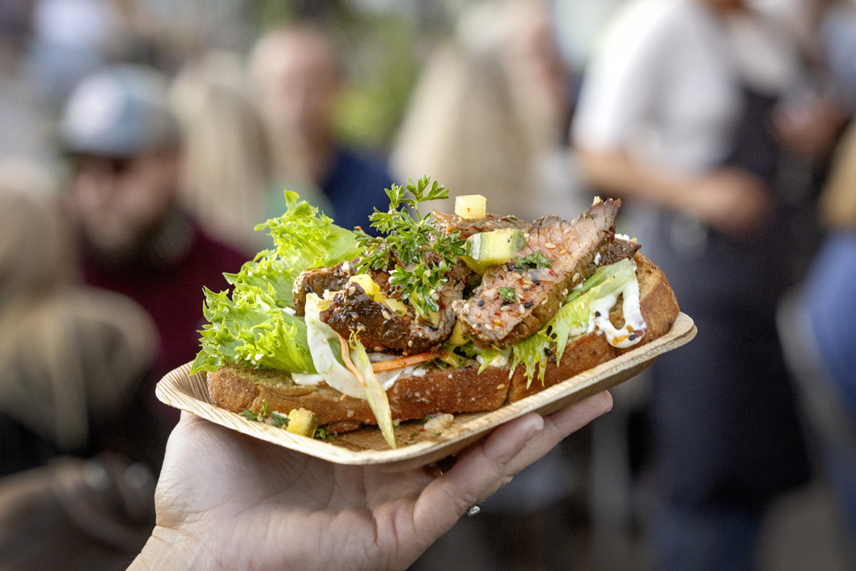 En hand håller upp en macka med kött och grönt.