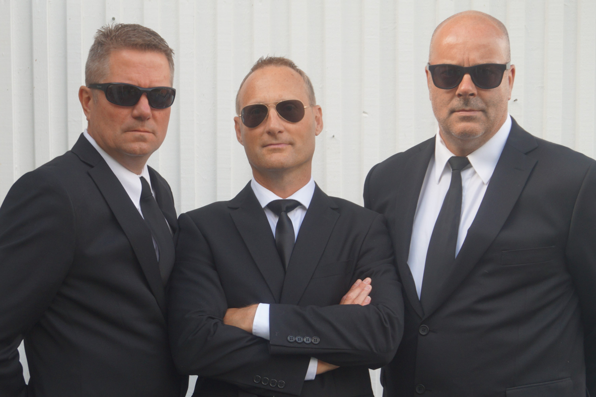 Tre män med svarta kostymer och solglasögon.