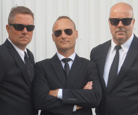 Tre män med svarta kostymer och solglasögon.