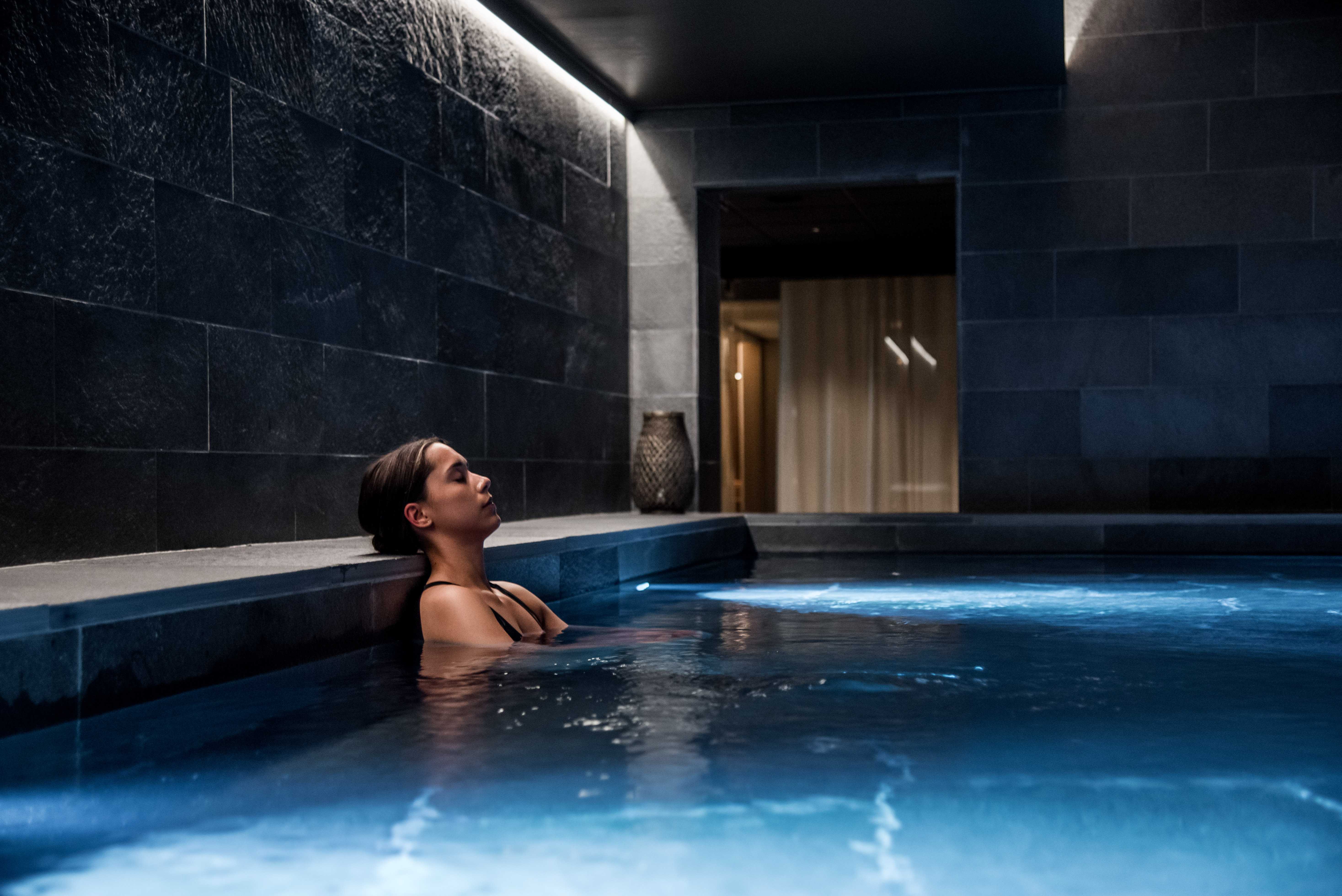 Kvinna i pool på spa, blundar och lutar sig mot poolkanten.