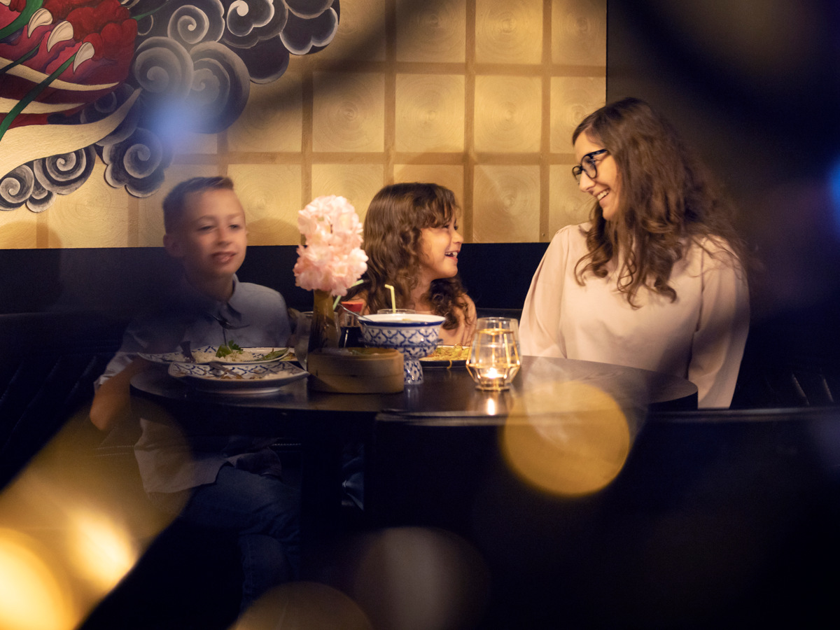 Två barn och en mamma äter mat på restaurang. 