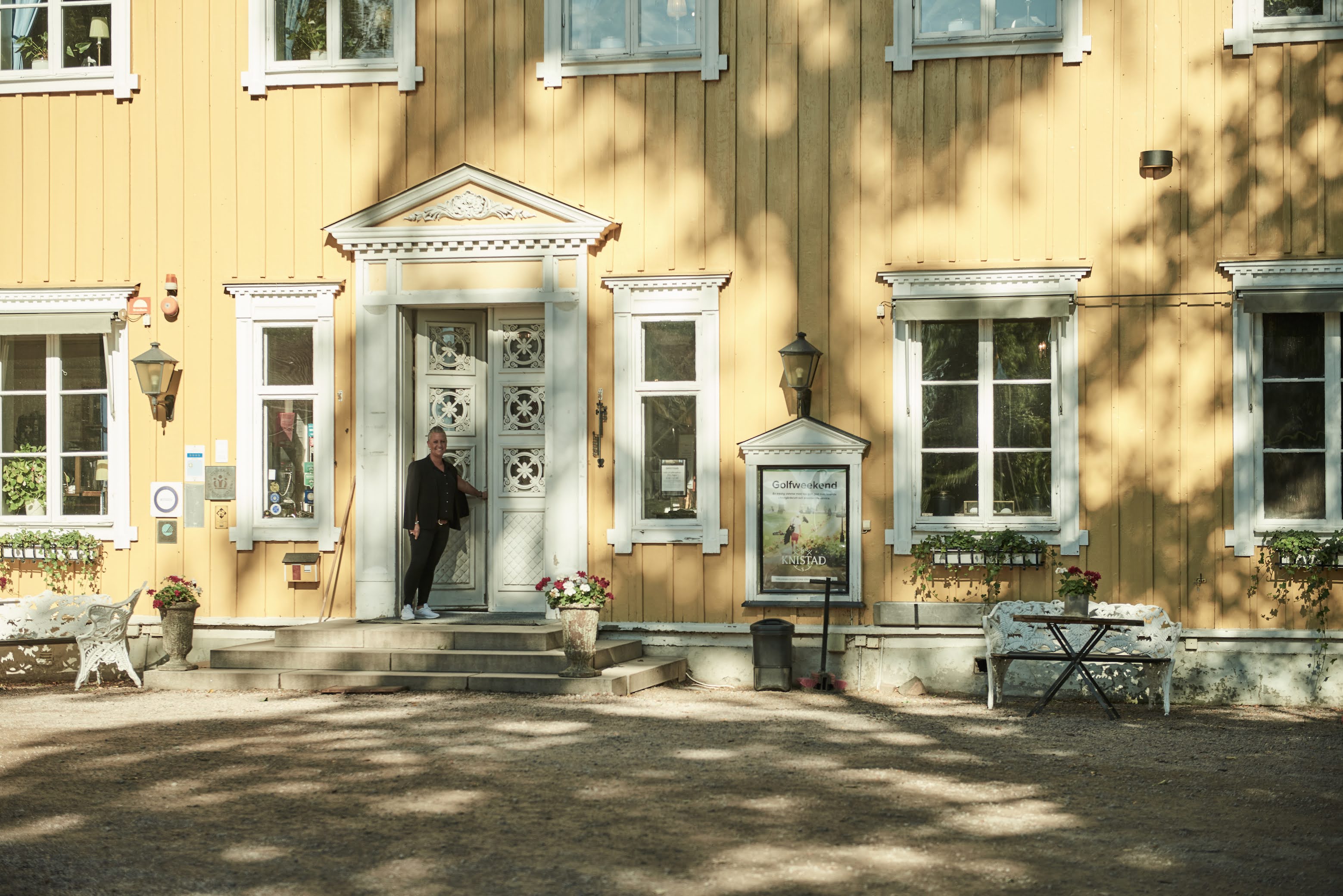 En kvinna är på väg in i ett stort vackert gult hus med vita trädetaljer. 