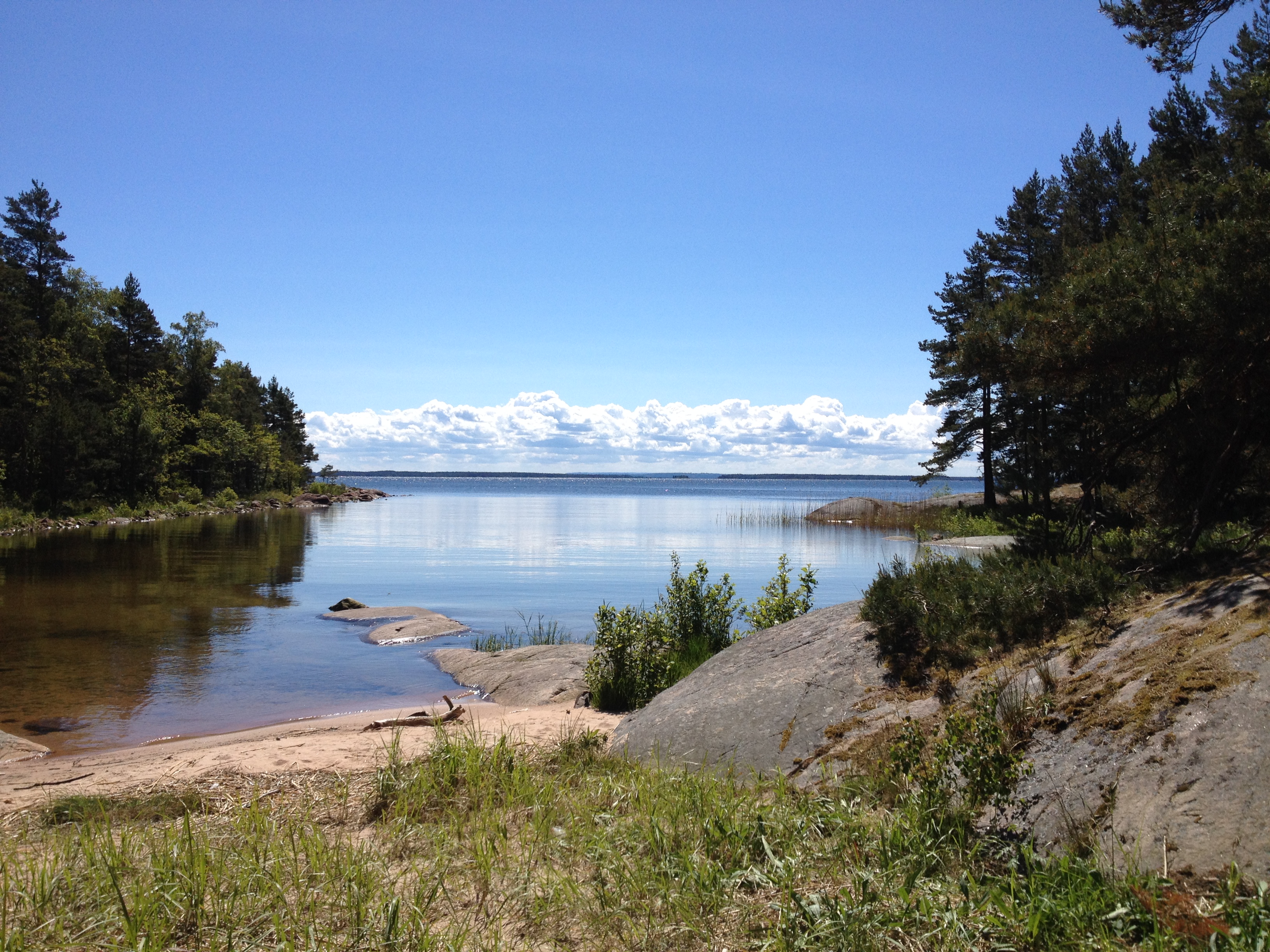 Vacker vy över en klippig strand. Vattnet ligger stilla under en klarblå himmel. 