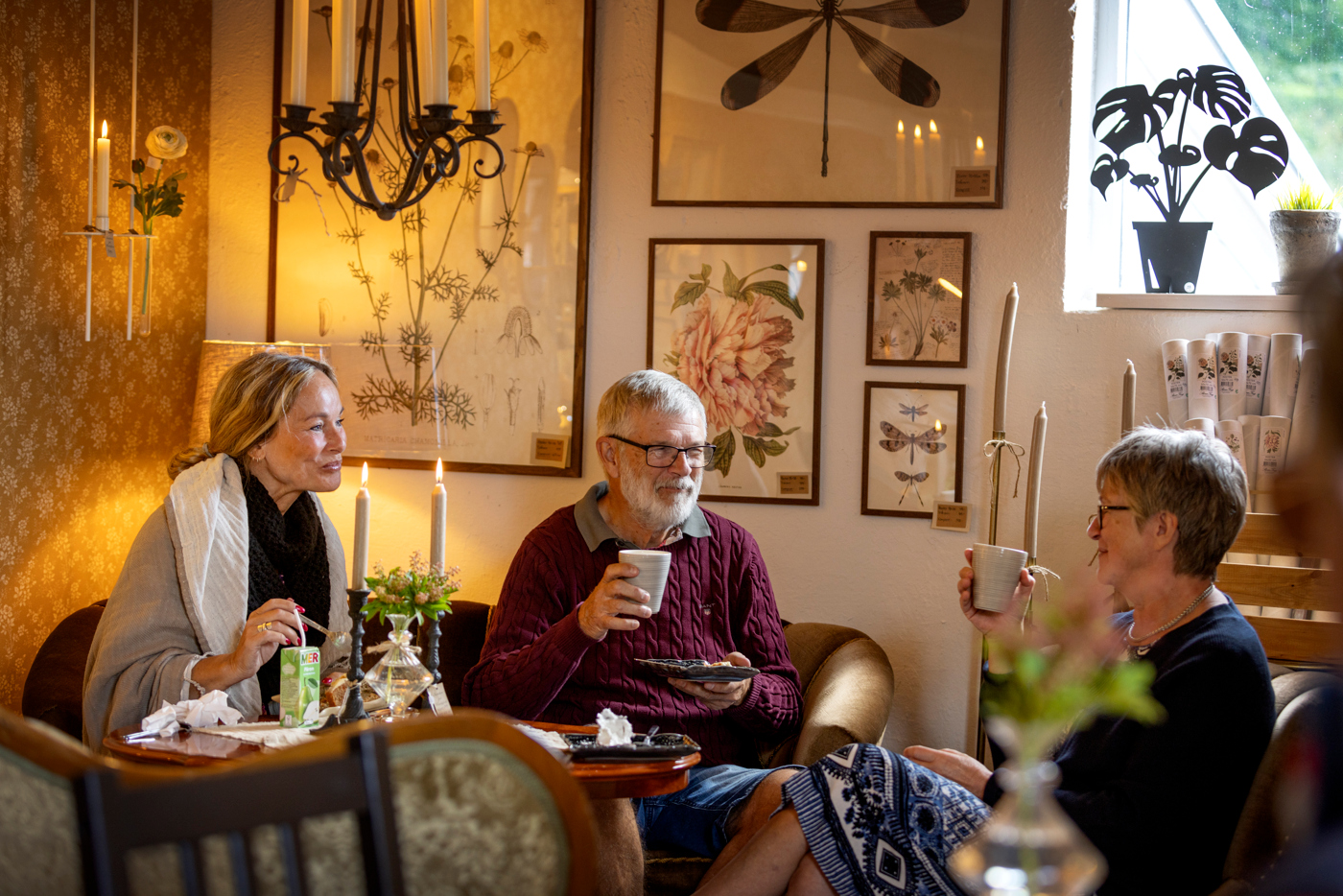 Två kvinnor och en man sitter och fikar i mysig miljö. 