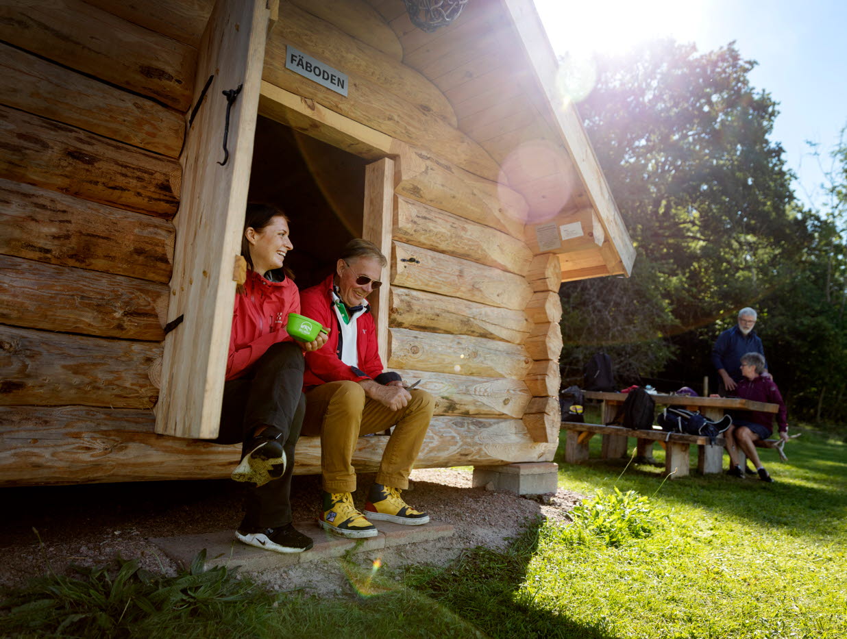 A woman and a man sit and rest by a shelter in the sunshine.