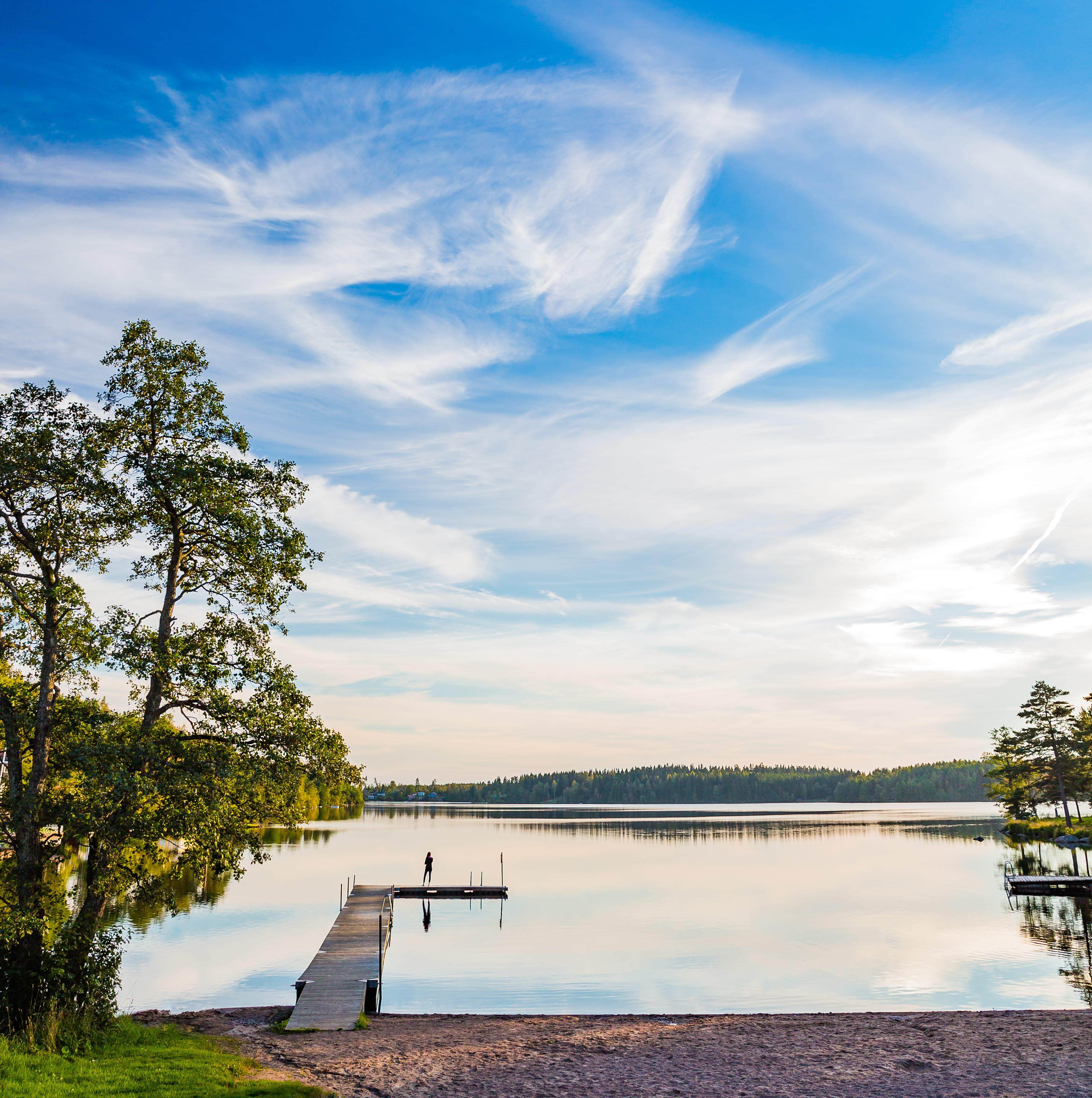 Utsikt över en brygga och en sjö med lätta moln och blå himmel. 