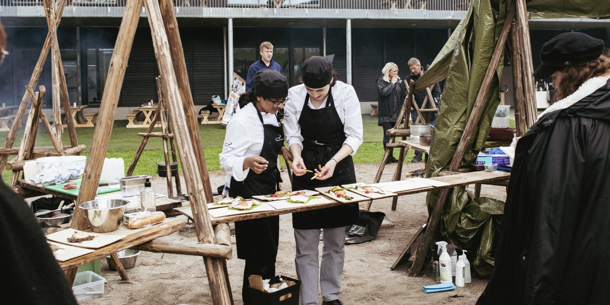 Två personer dekorerar tallrikar på en matlagningstävling utomhus. 